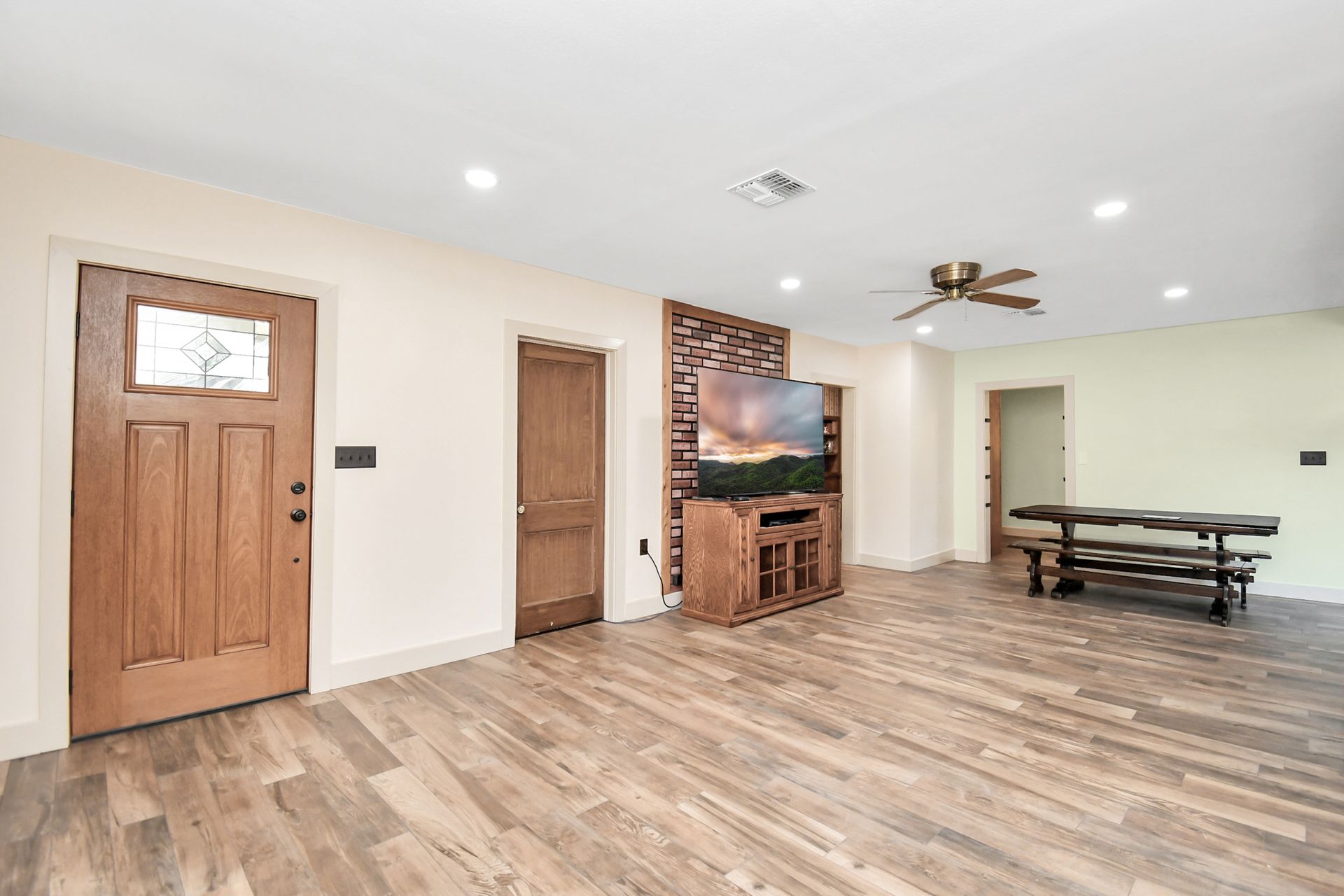 Spacious living room with wood floors, wooden doors, large TV, and a bench.