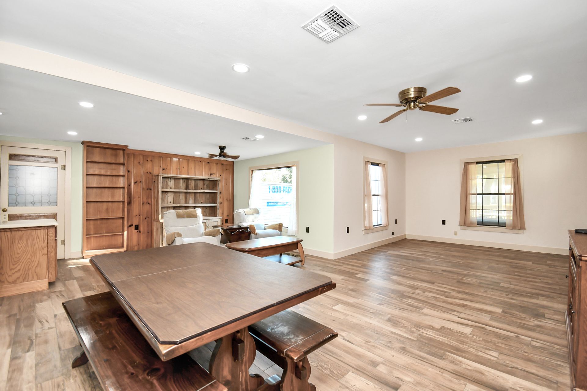 Spacious open-plan dining area with a large wooden table and benches, hardwood floors, and built-in shelving.