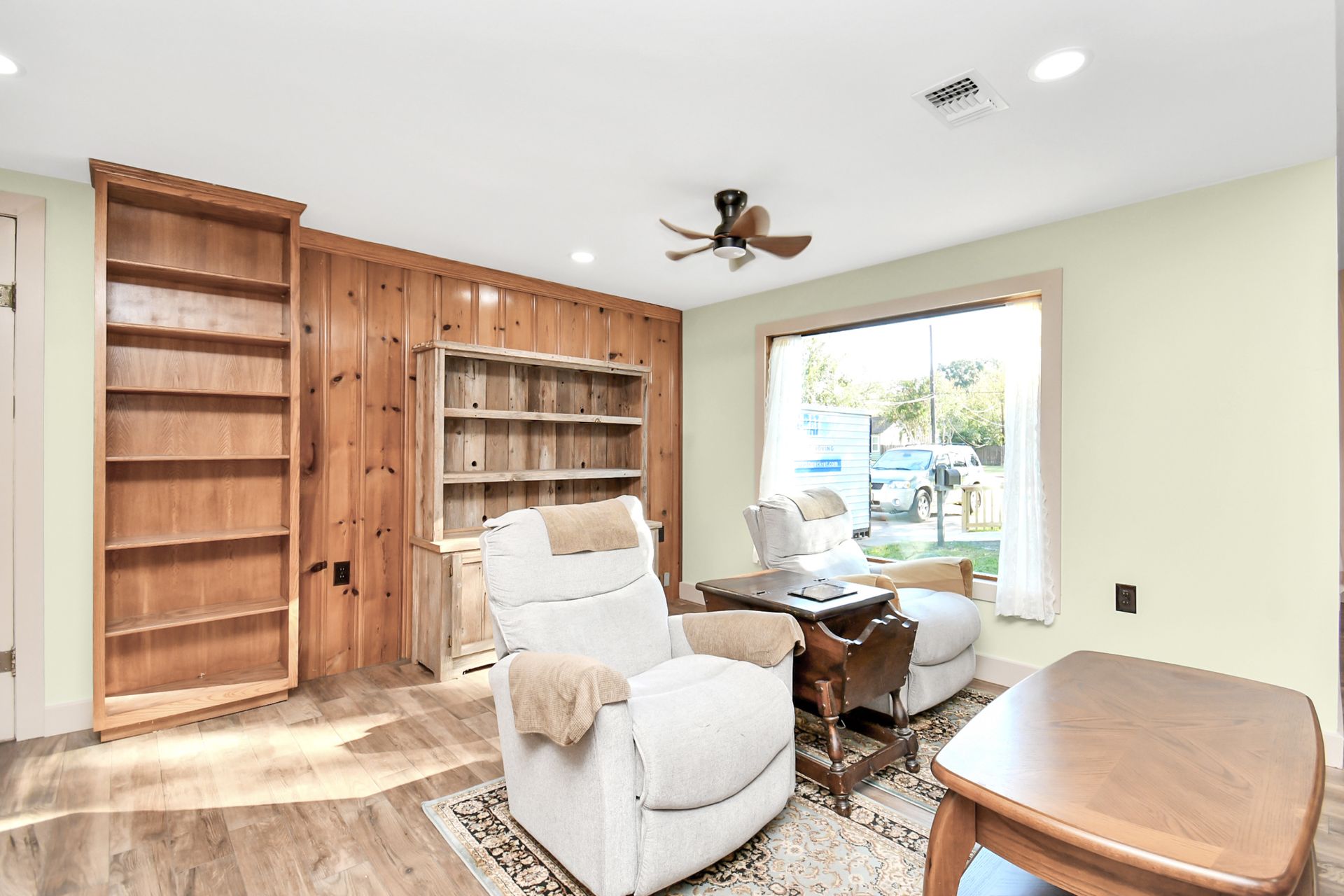 Living room with recliner, bookshelves, wood paneling, window, and ceiling fan.