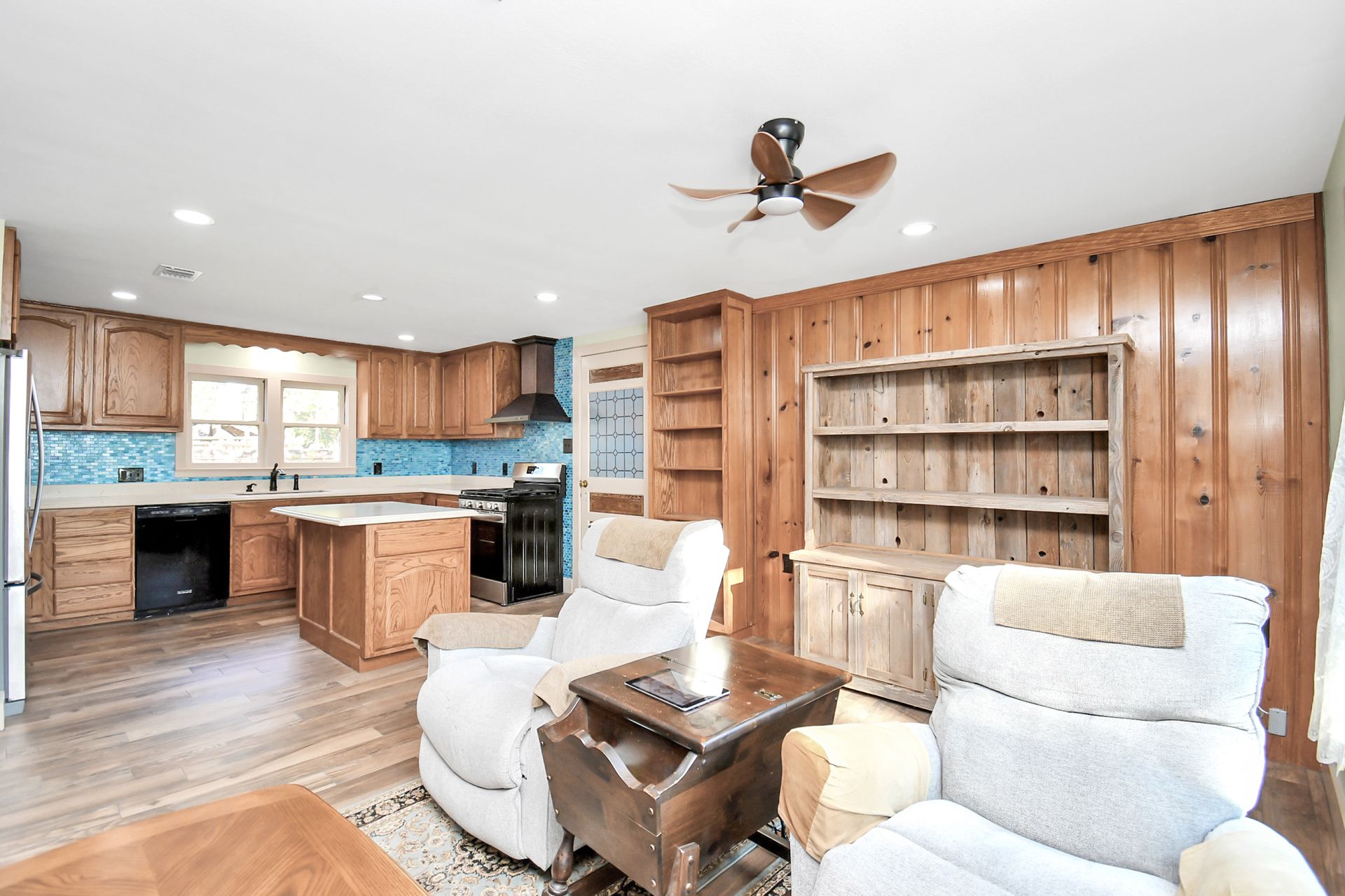 Open-concept living space with kitchen, wood paneling, two recliners, and built-in shelving.