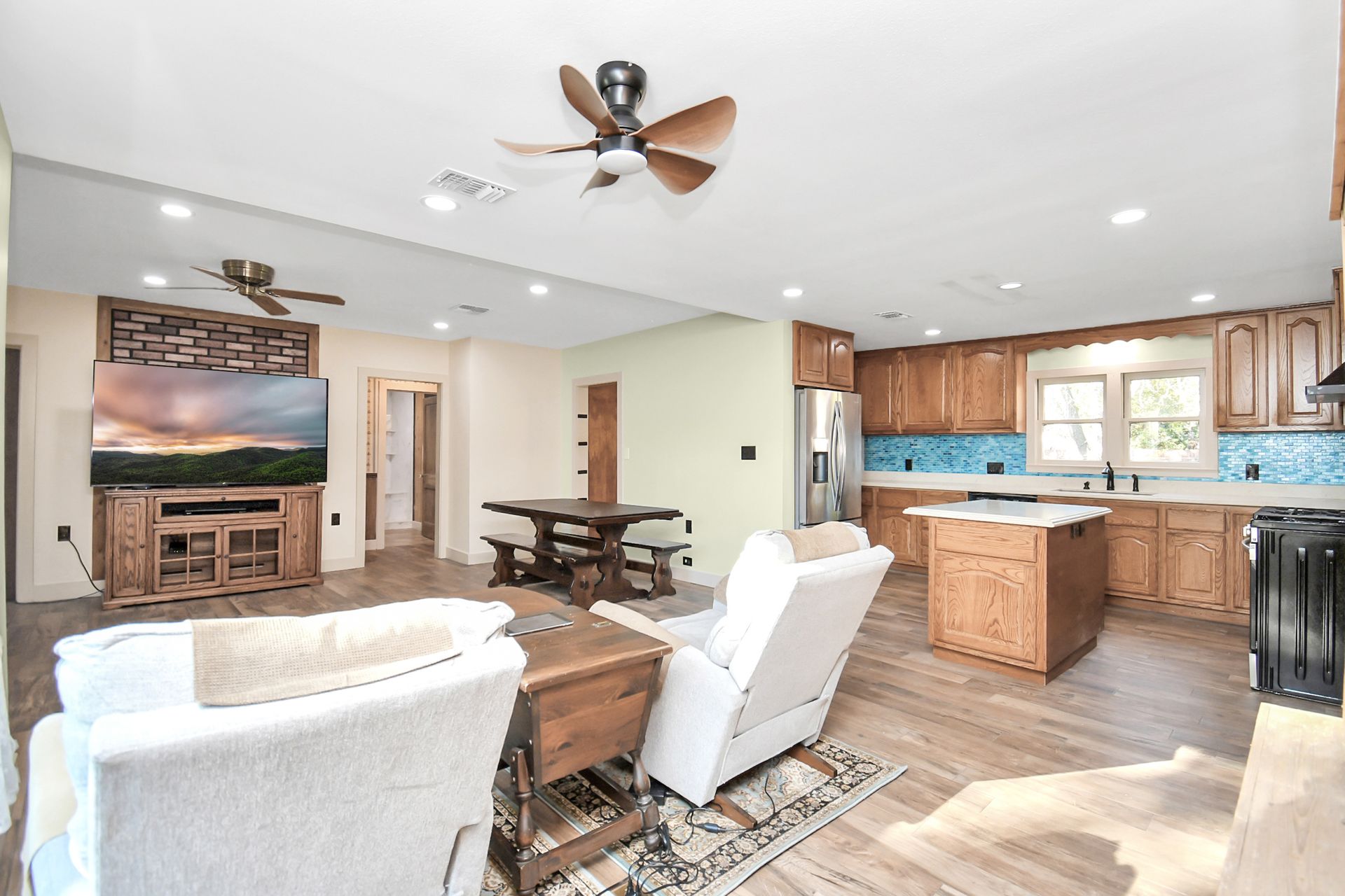 Open-concept living space with kitchen, dining, and living areas. Wooden floors, light walls, and natural wood cabinets.