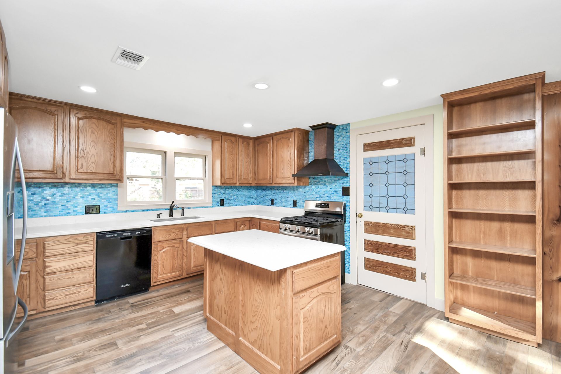 Kitchen with oak cabinets, blue tile backsplash, island, and wooden floor.