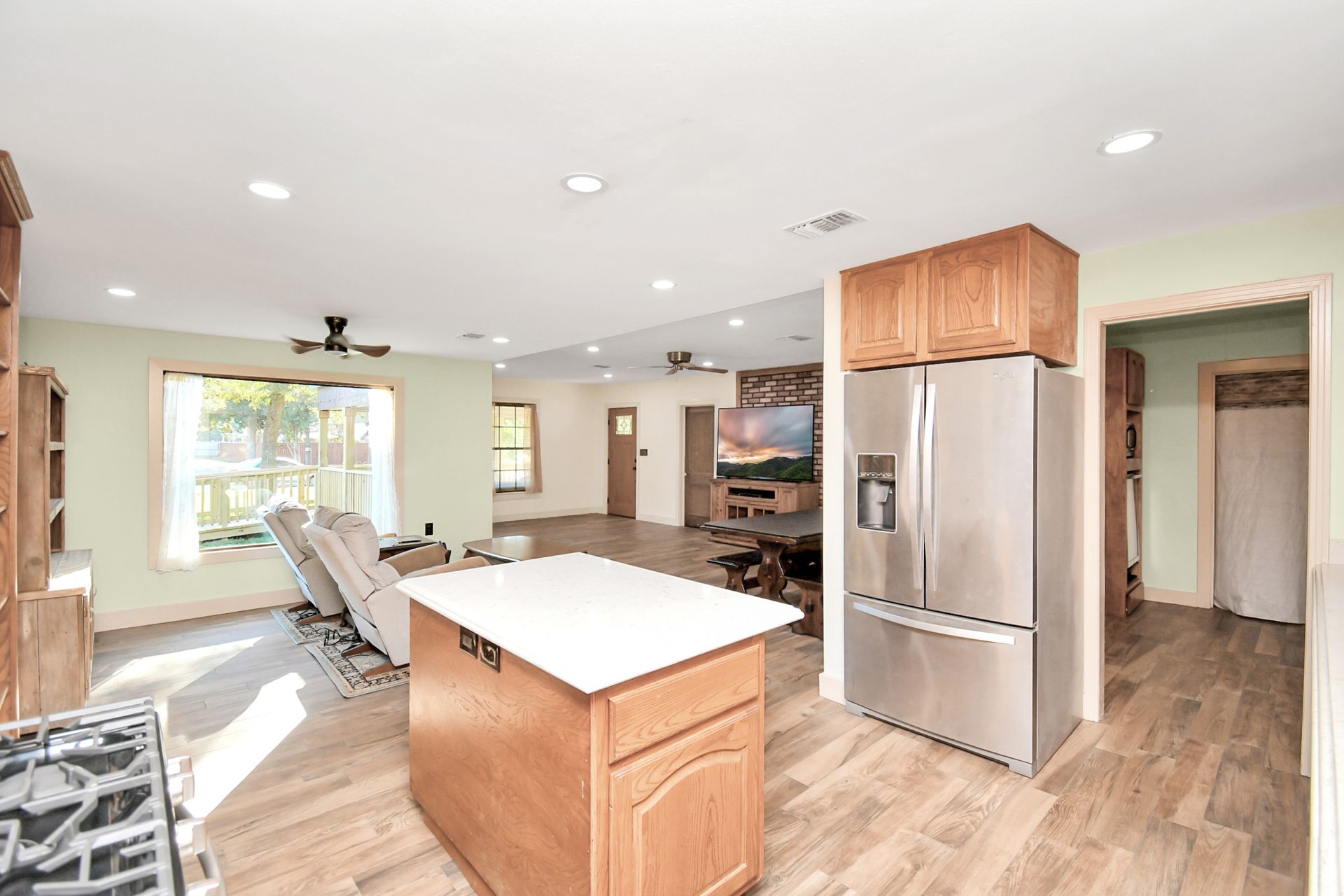 Open-concept kitchen and living area with wooden cabinets, stainless steel appliances, and light wood floors.