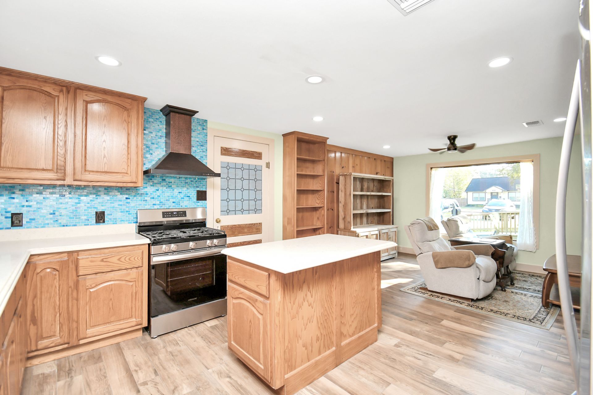 Open-concept kitchen with wooden cabinets, blue tile backsplash, stainless steel appliances, and a cozy living area.