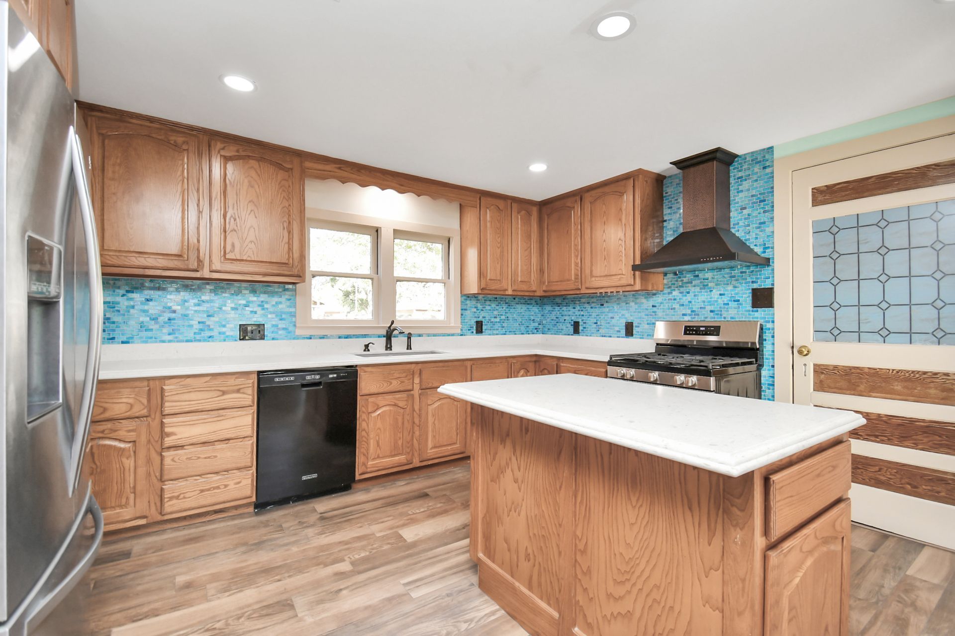 Kitchen with light wood cabinets, blue tile backsplash, stainless steel appliances, and a white island.