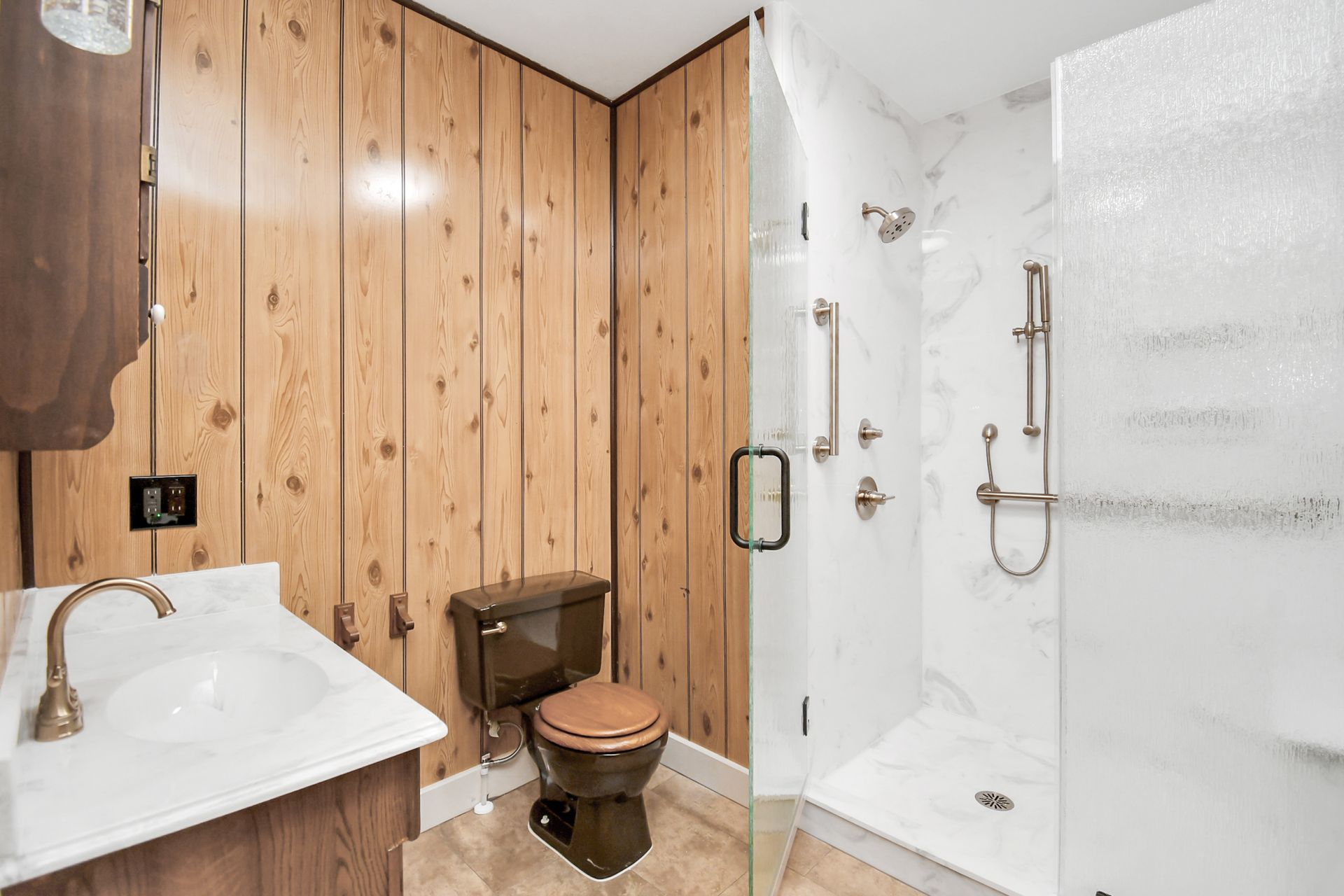 Bathroom with wood paneling, a dark toilet, a white shower with marble effect, and a white sink.