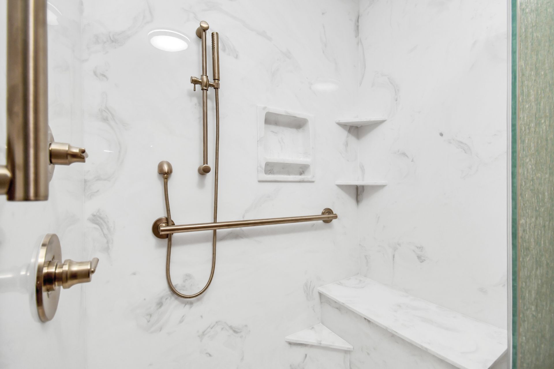 A white marble-look shower with grab bar, showerhead, built-in shelves, and seat.