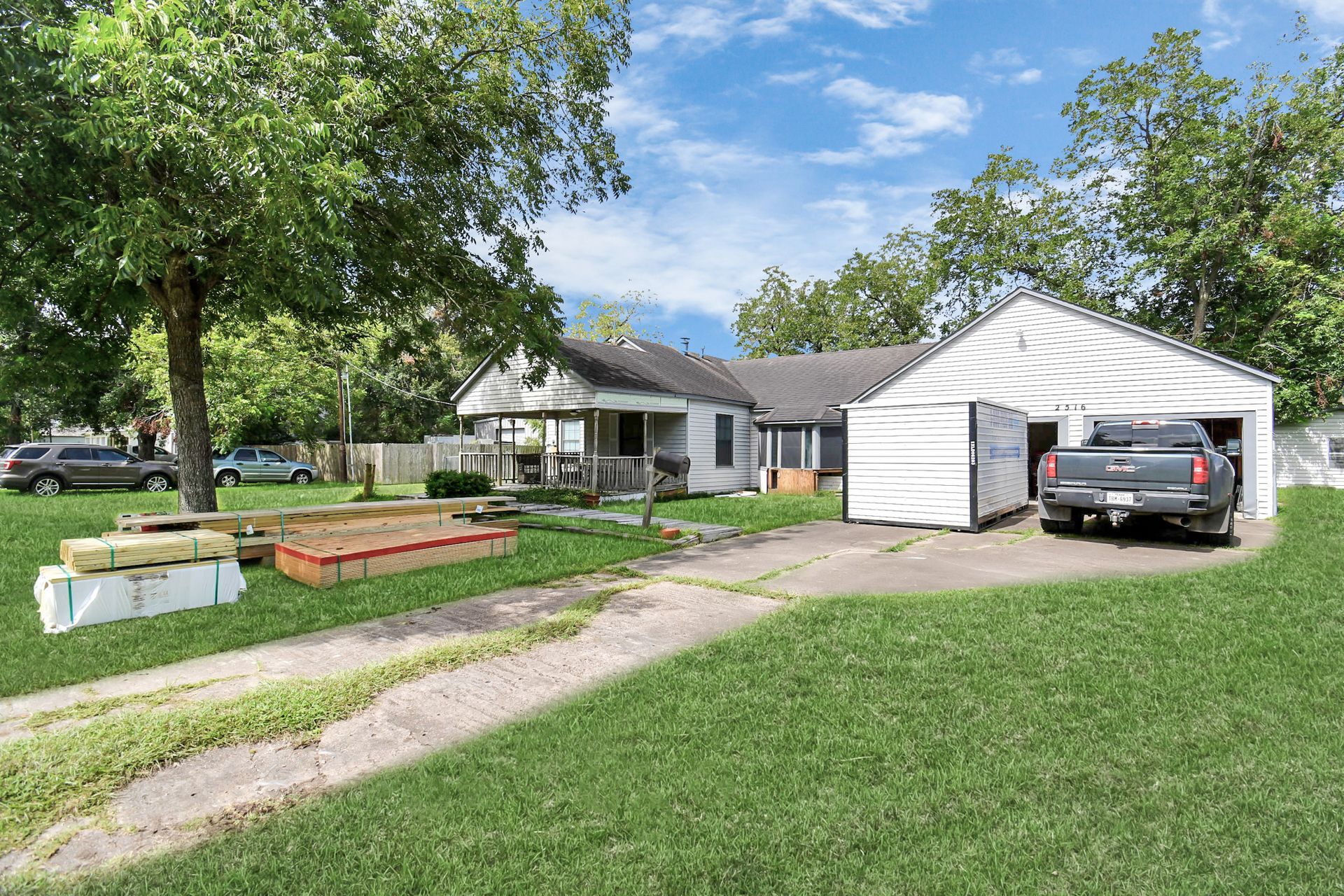 House with driveway, garage, and yard. Truck parked in the garage. Lumber on the lawn.