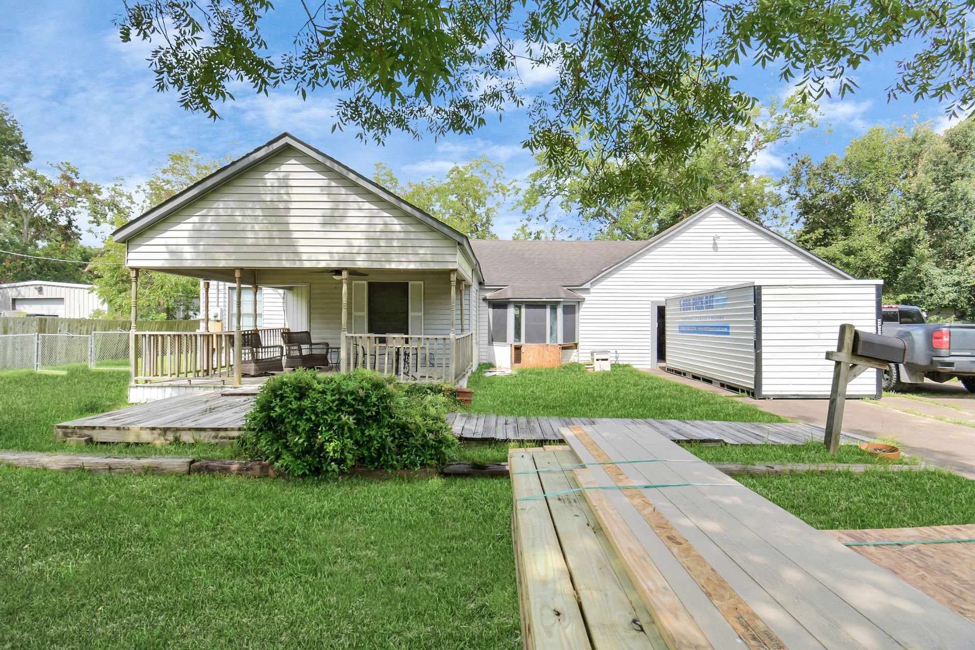A weathered house with a porch, wooden walkway, and green lawn under a blue sky.