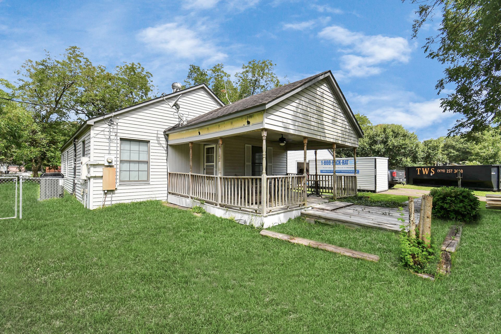 Dilapidated, white house with porch and overgrown lawn under a blue sky.