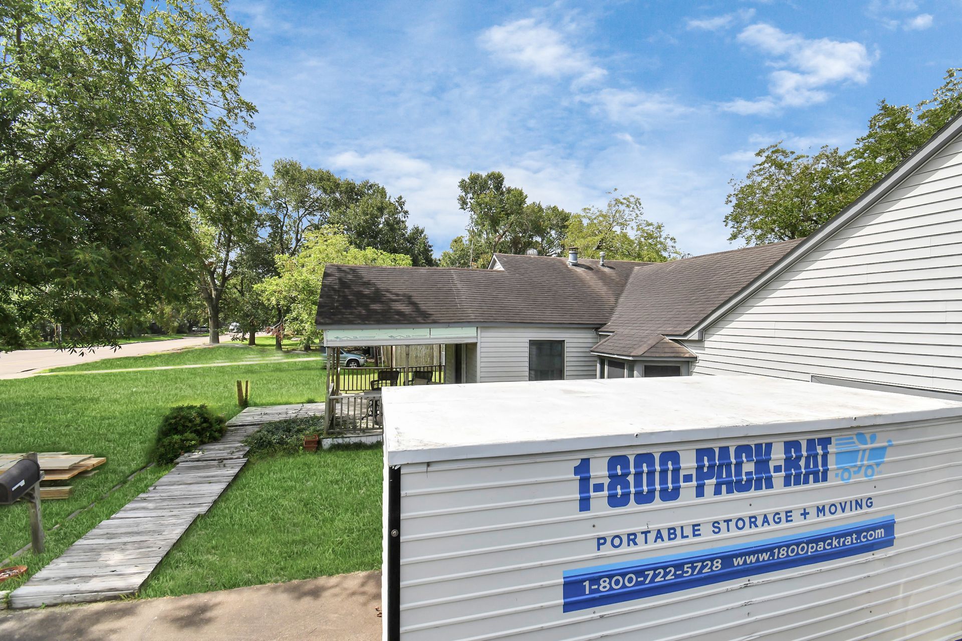 A white moving container in front of a house with a grassy yard and sidewalk.
