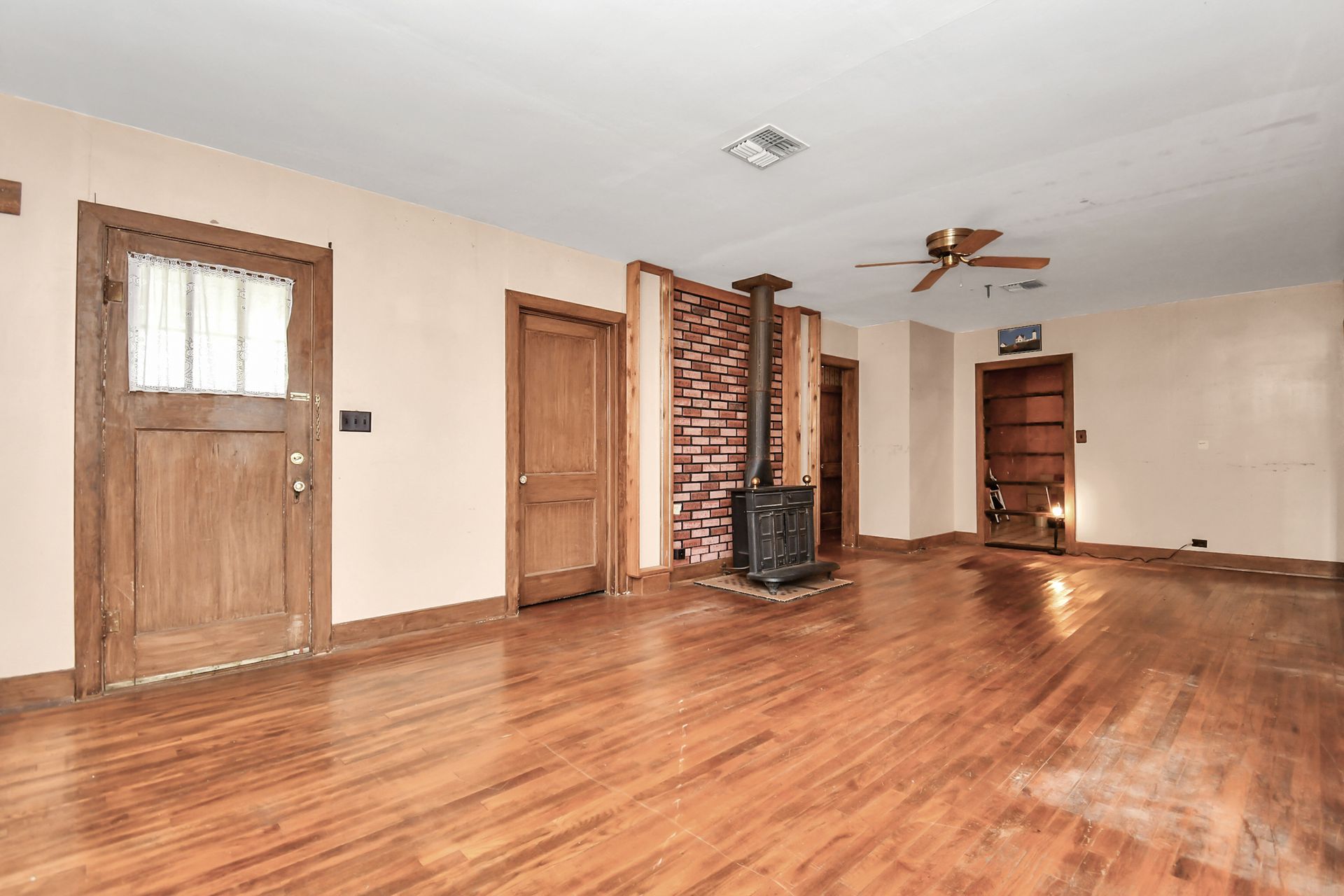 Empty room with hardwood floors, wood doors, a brick chimney, and a ceiling fan.