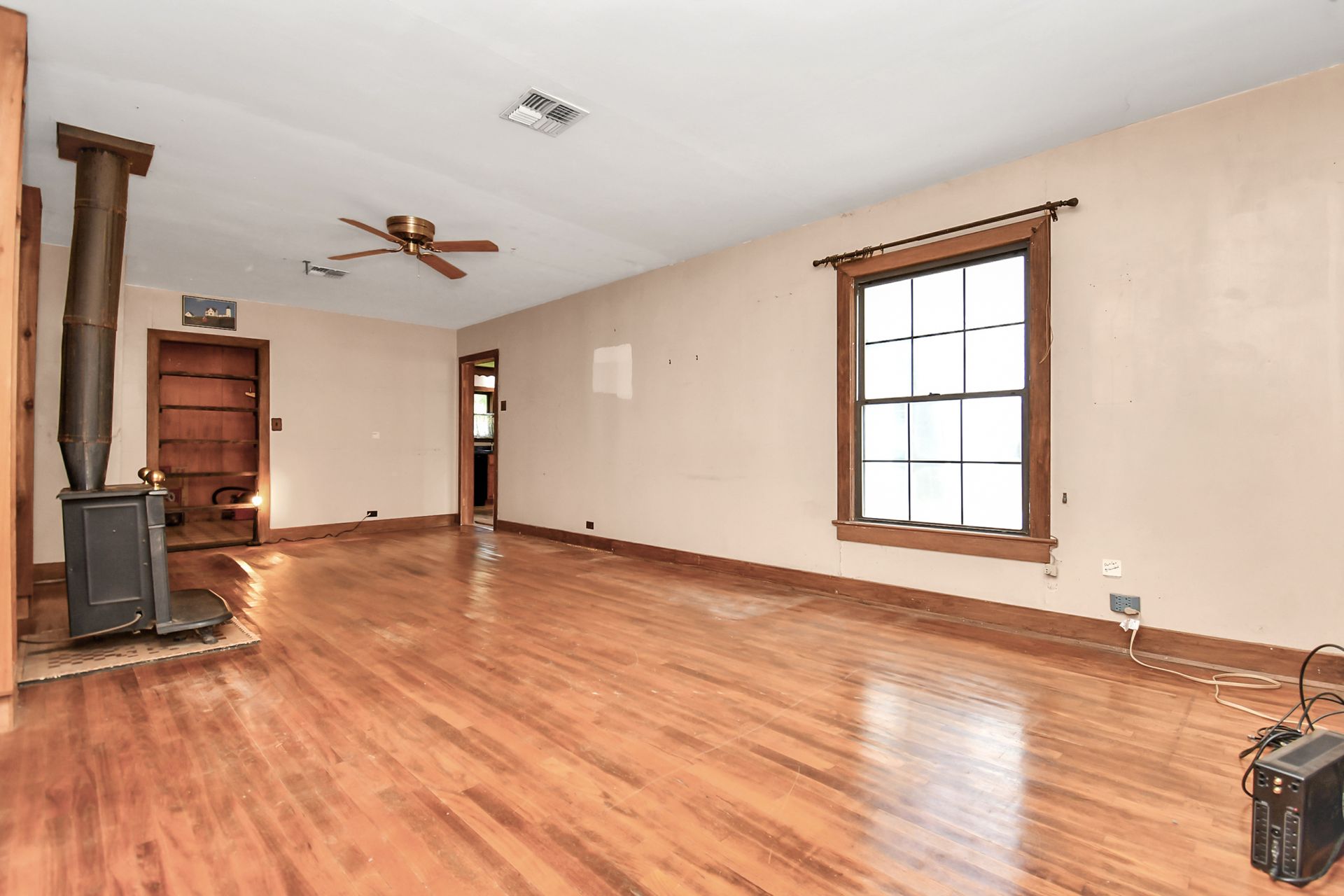 Empty living room with hardwood floors, wood stove, and window.