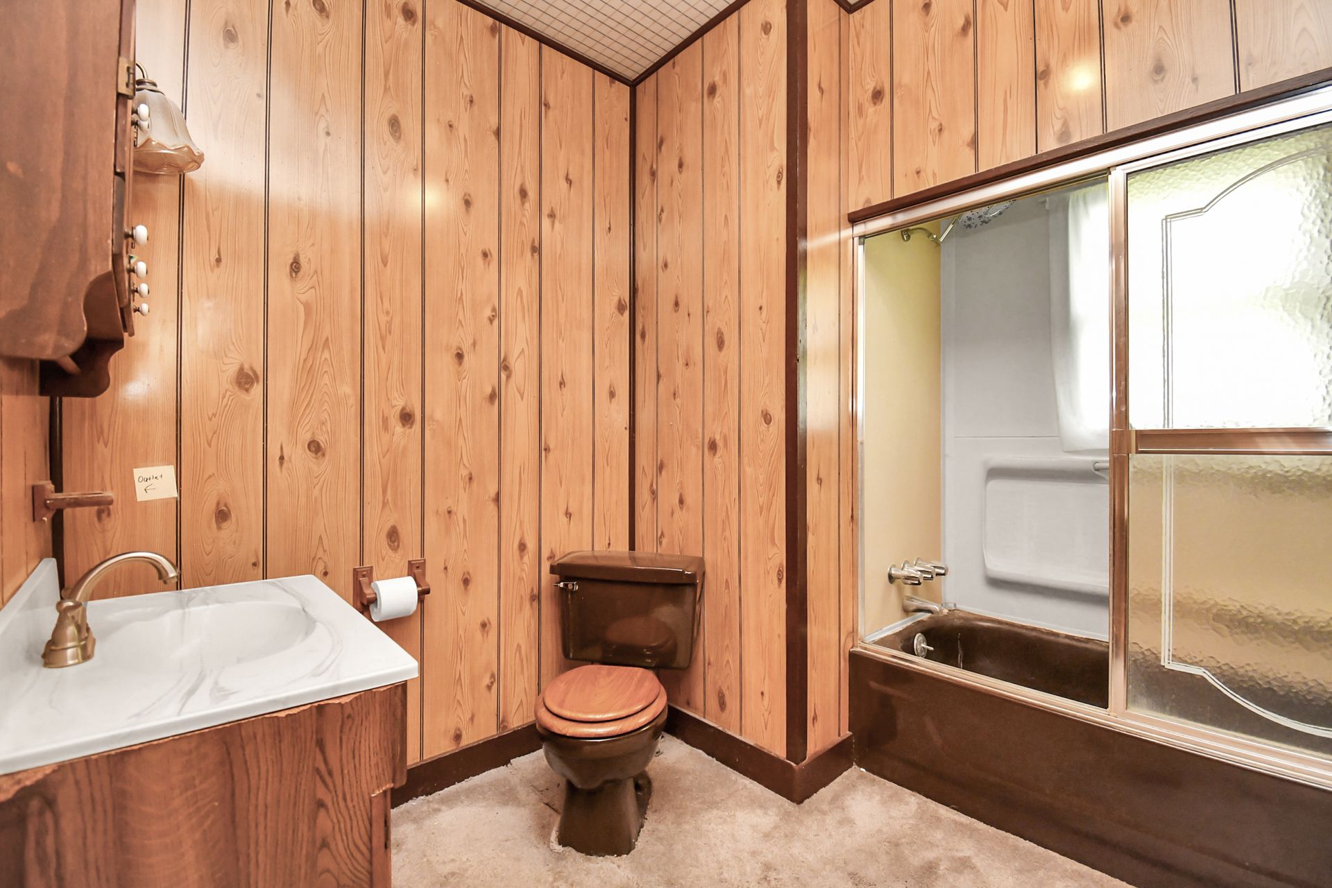 Bathroom with wood paneling, brown toilet and vanity, tub with shower curtain, and white sink.