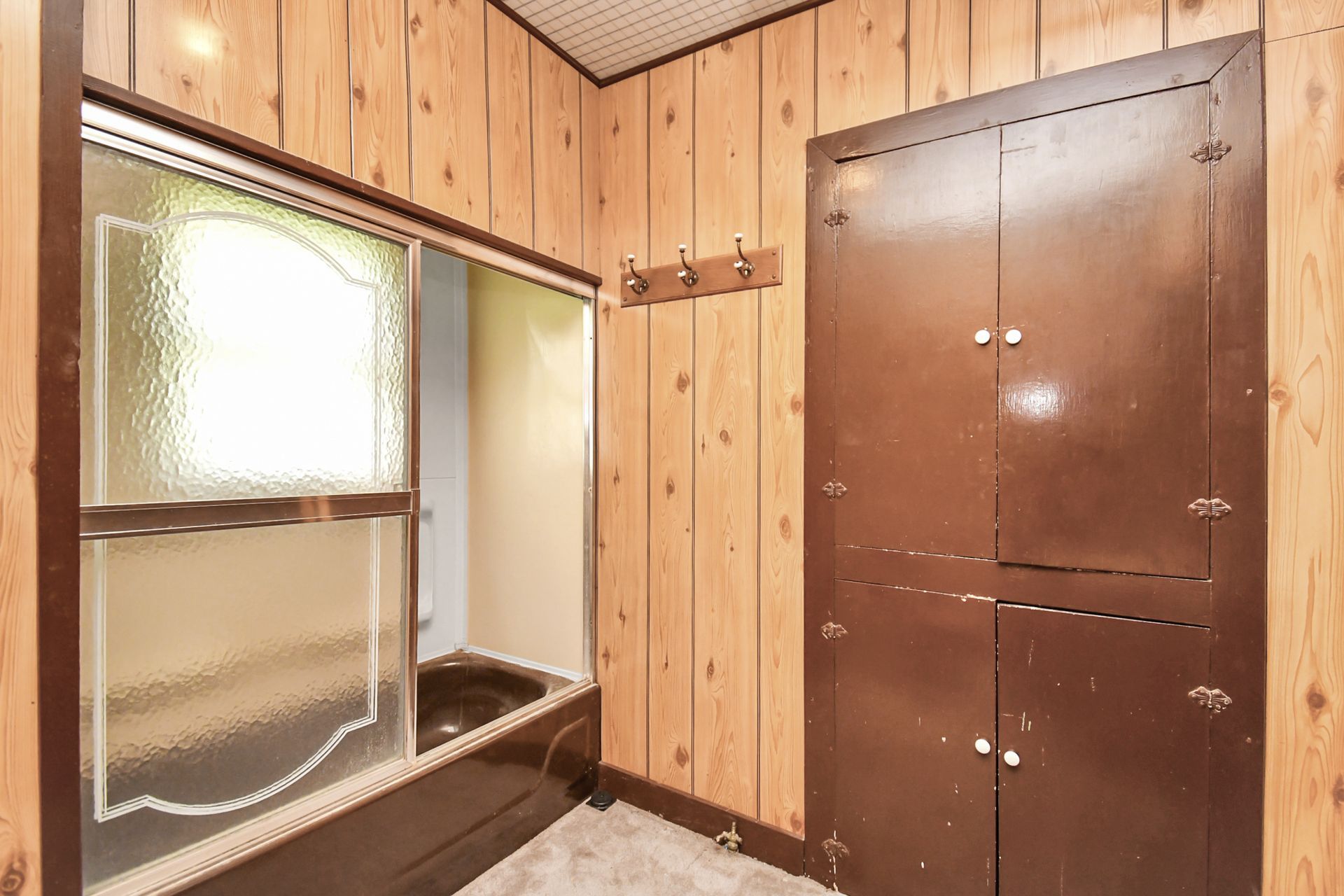 Bathroom with wood paneling, brown cabinet, shower with glass door, and white ceiling.