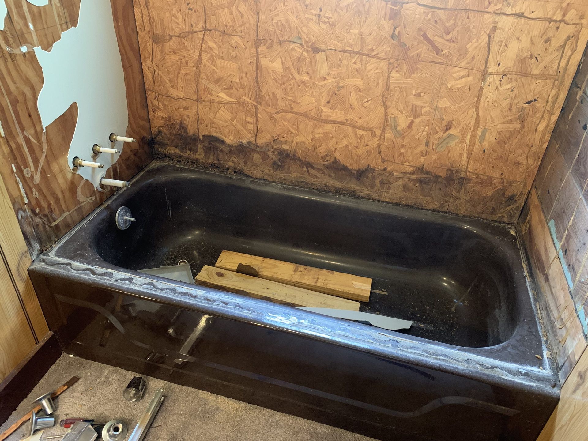 Bathtub with water fixtures and exposed wall behind. Dark tub, wood boards inside.