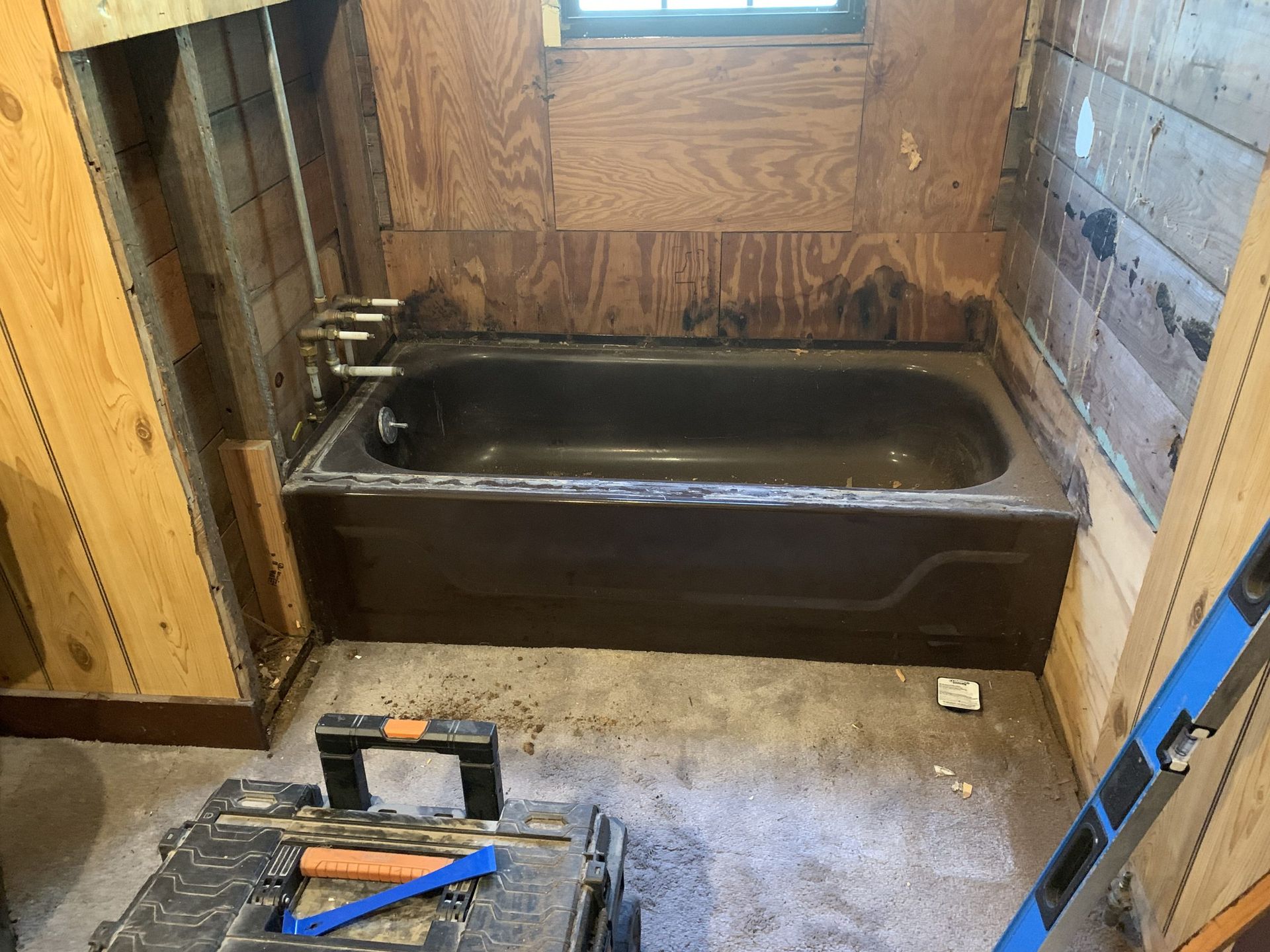 Bathroom under renovation with dark tub, exposed framing, tools on floor.