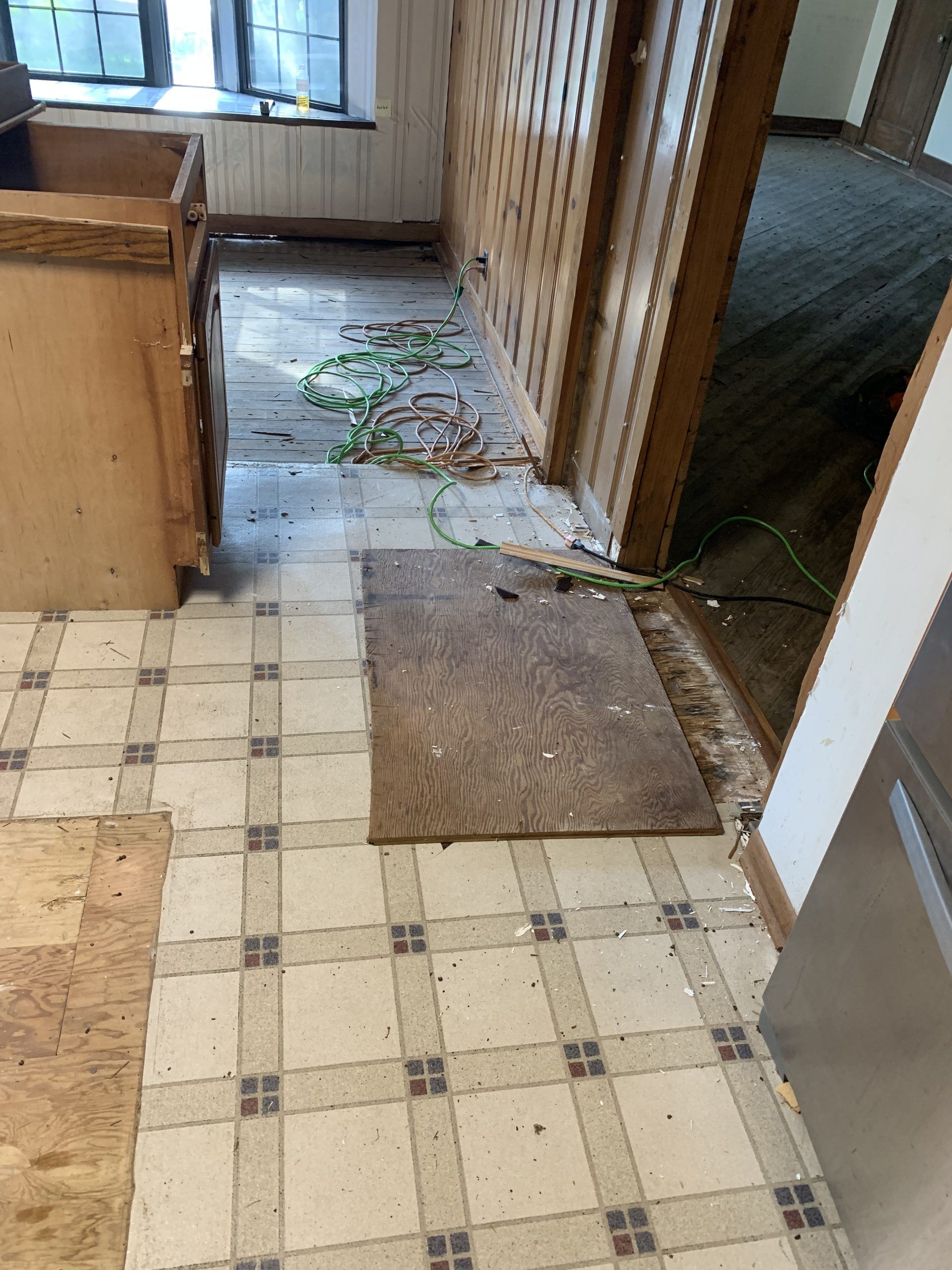 Kitchen with damaged flooring, cabinet, doorway, and debris.