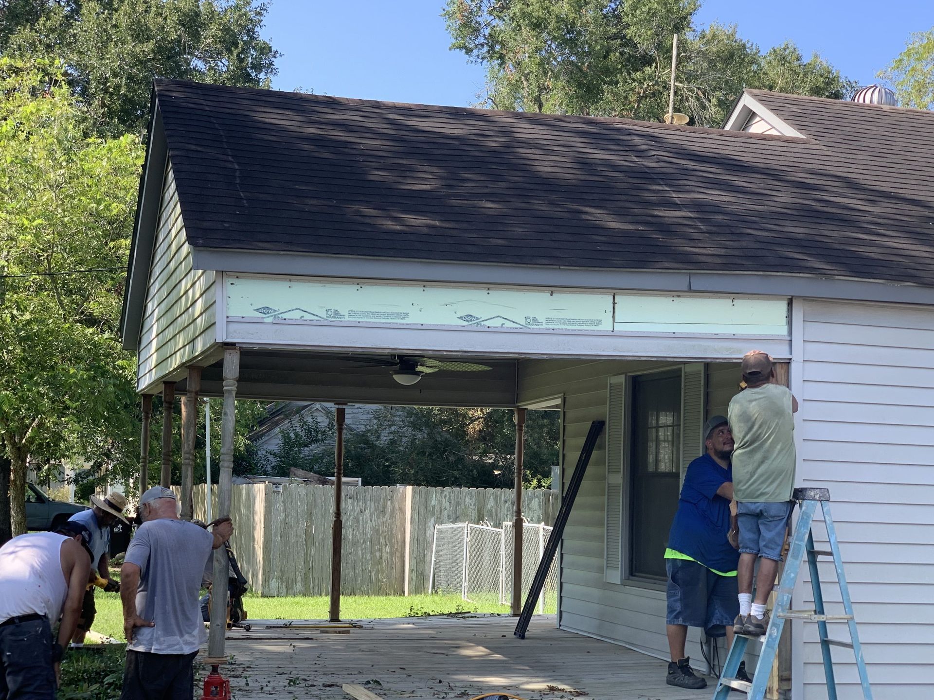 Construction workers removing a porch roof. Several men in various positions near the structure, with the roof in view.