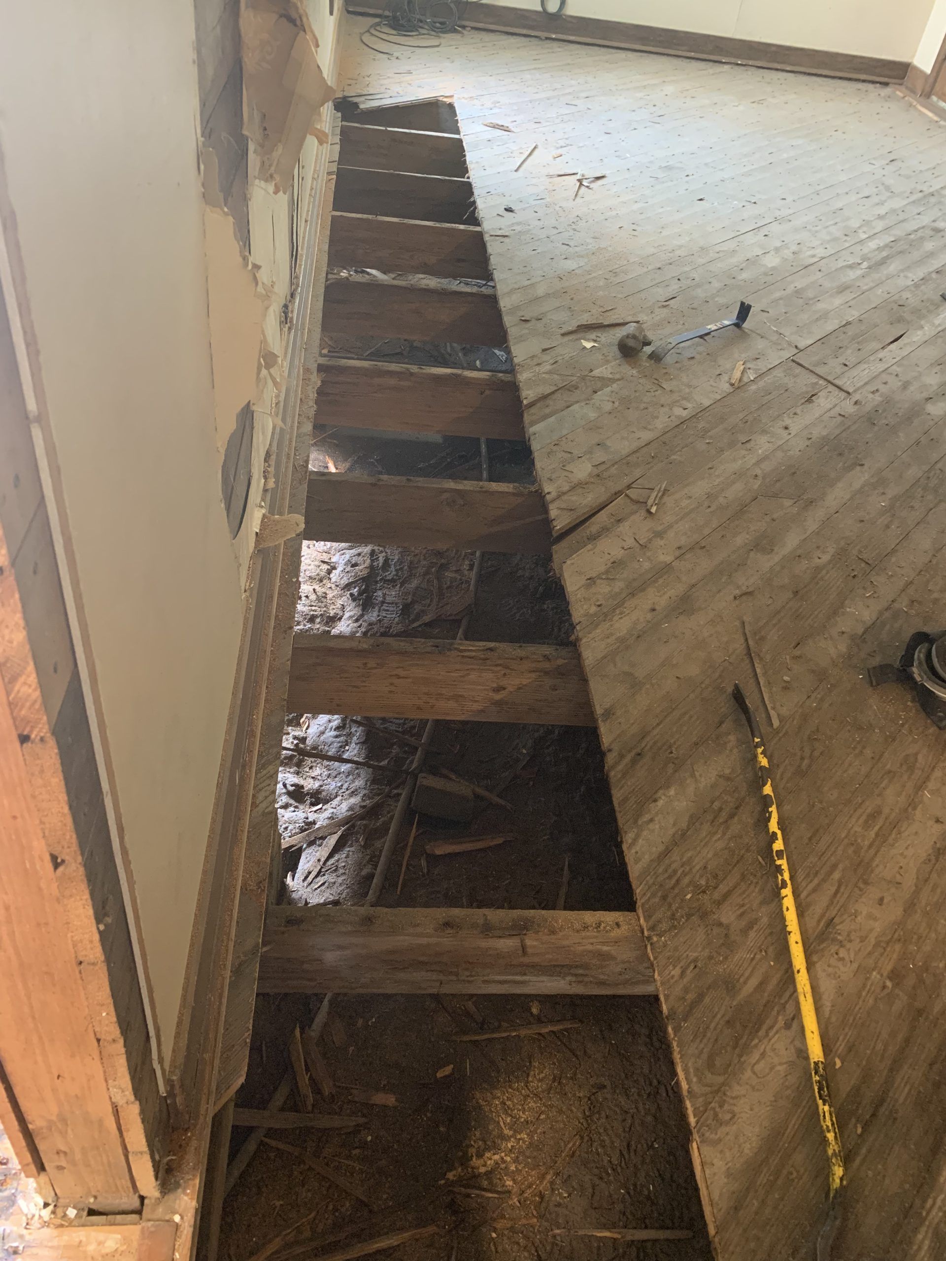 A floor ripped open, revealing wooden joists, debris. Interior, construction.