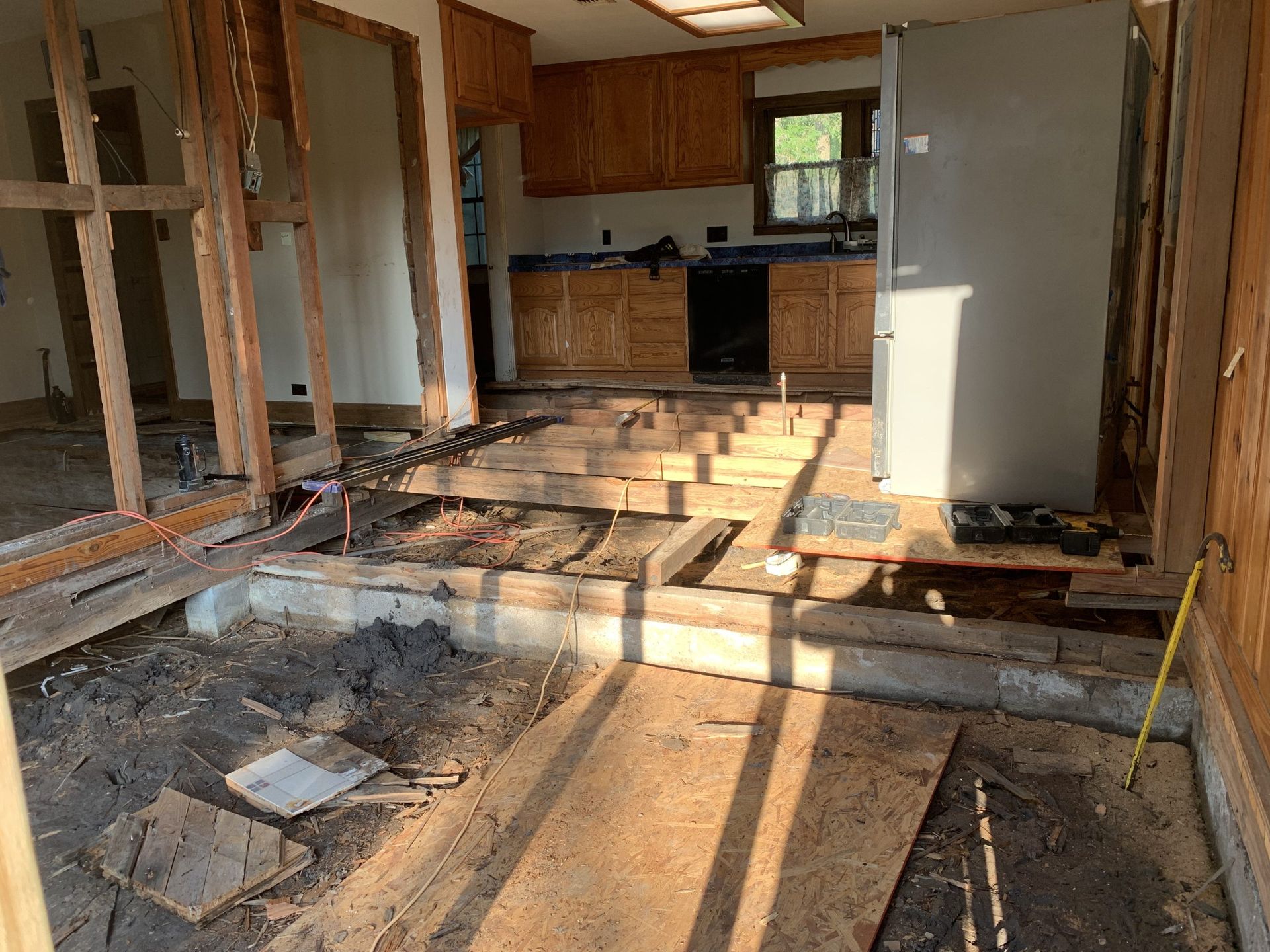 Kitchen undergoing renovation: exposed floorboards, cabinets, bare walls, and construction materials.