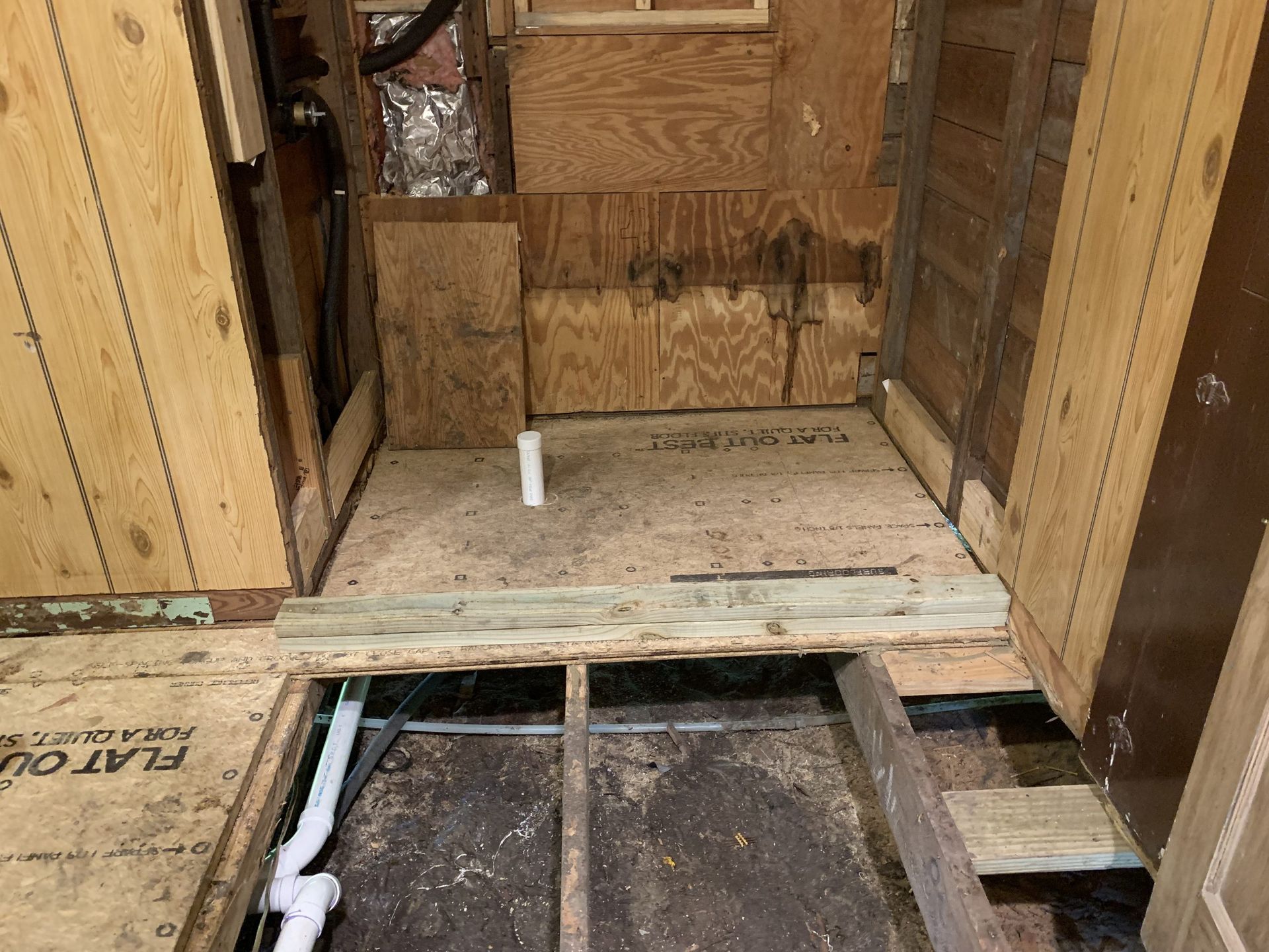 Bathroom under renovation. Exposed framing and subfloor with plumbing visible.