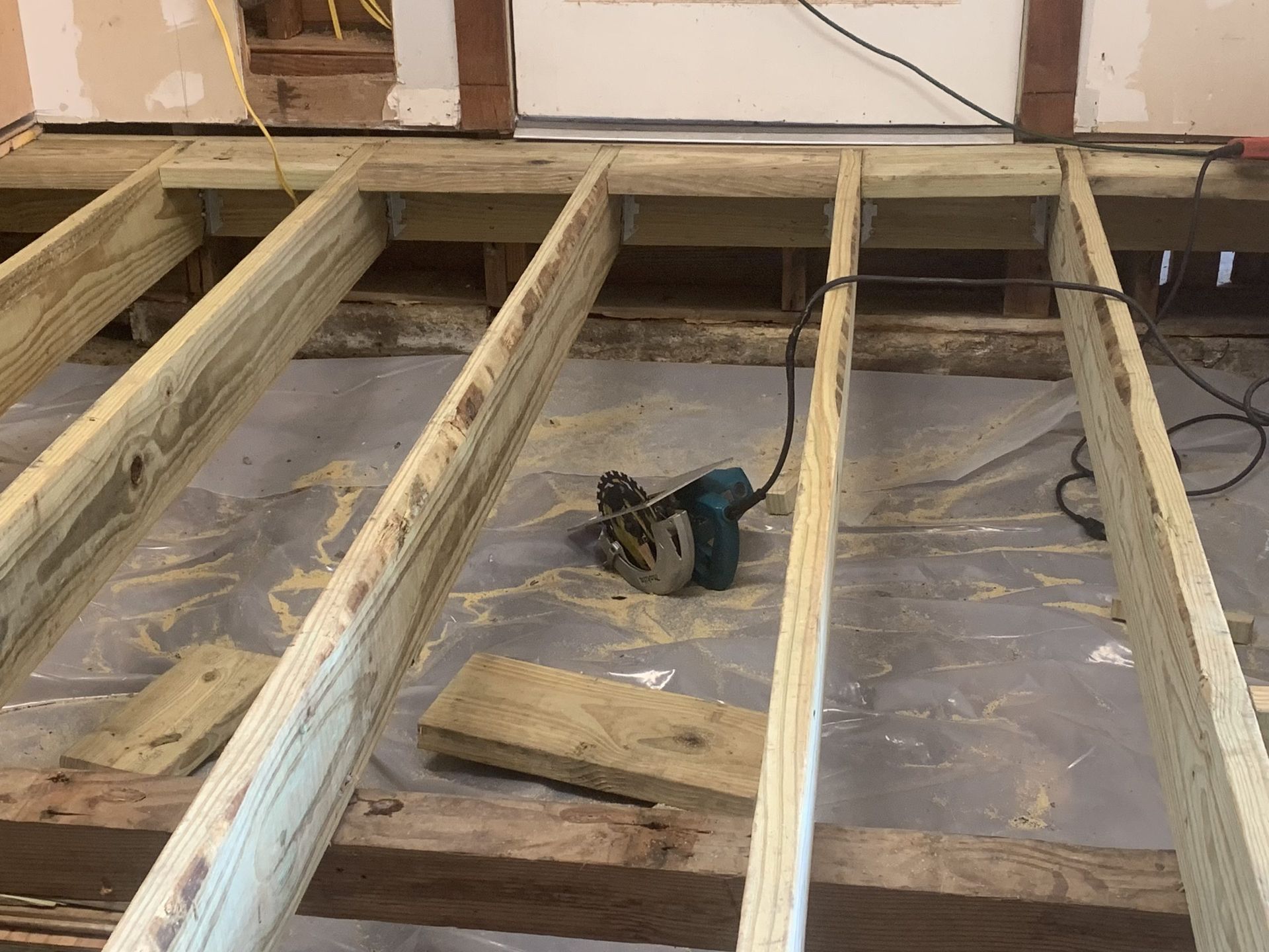 New floor framing with a circular saw on the concrete floor, with old framing visible in a room.