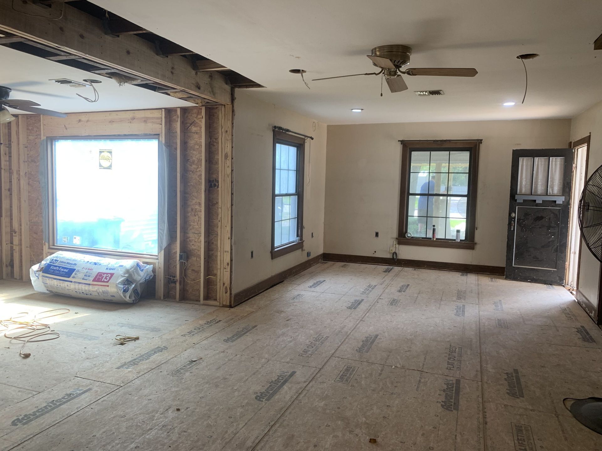 Interior room under renovation with exposed framing, windows, and a ceiling fan.