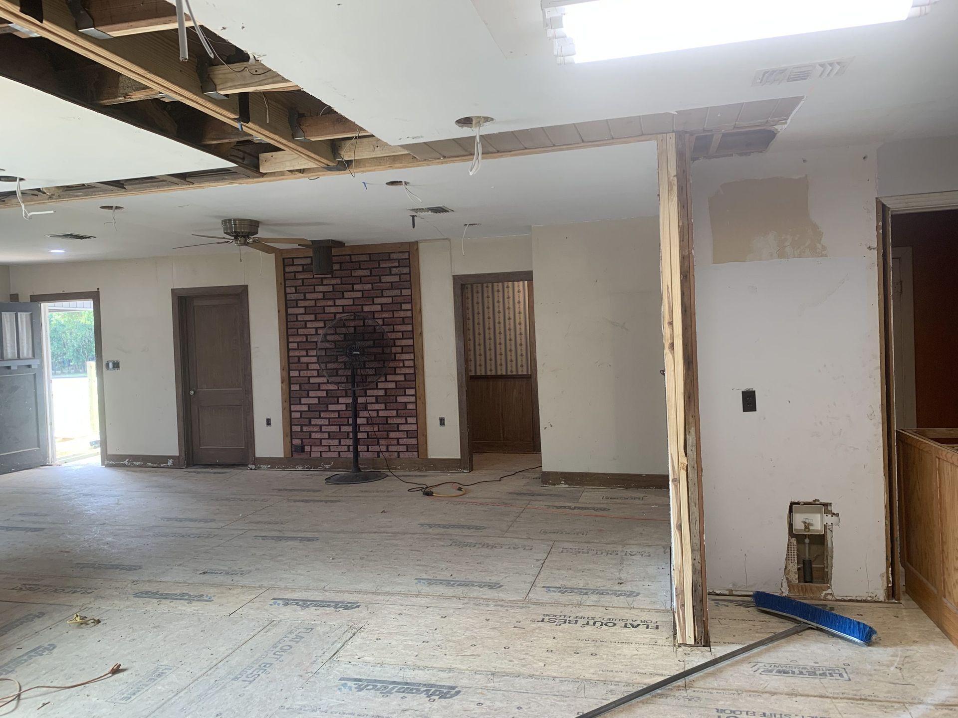 Interior view of a room under renovation, with exposed ceiling beams and a brick accent wall.