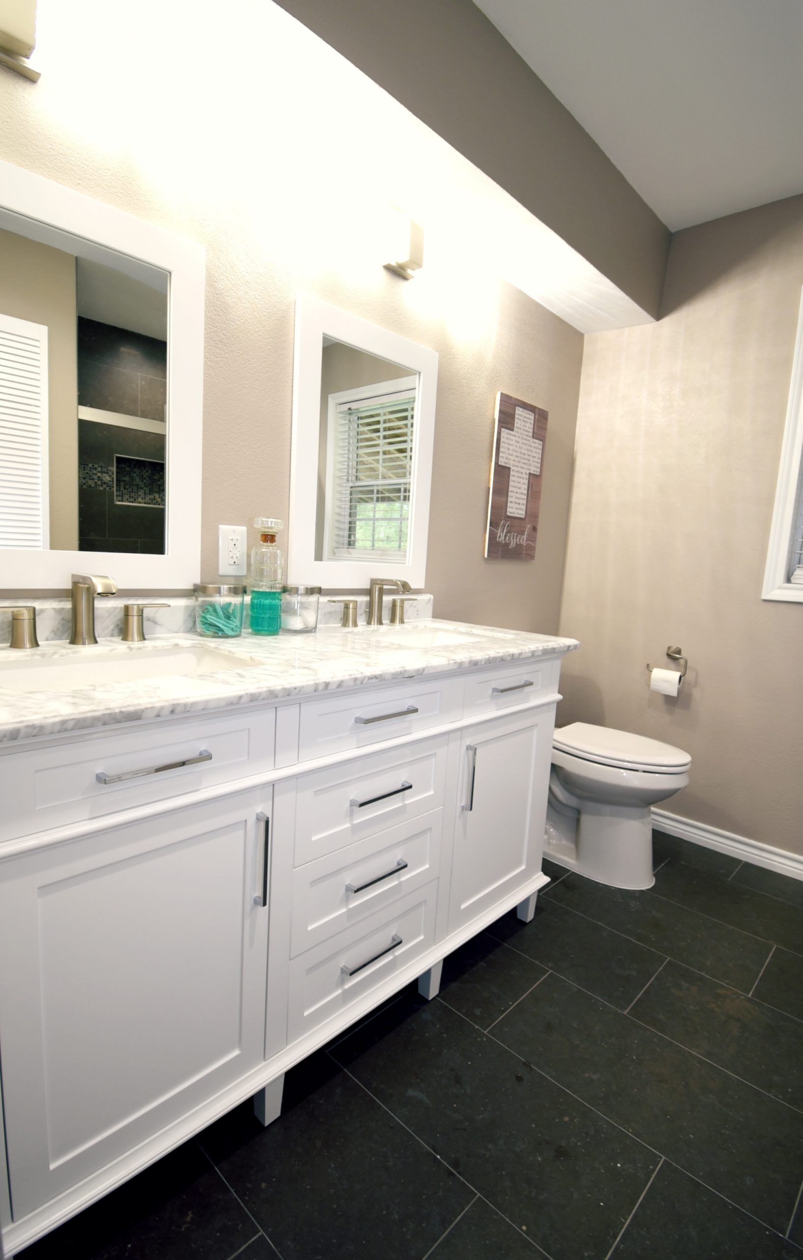 White double vanity bathroom with marble top, two mirrors, and dark tile floor.