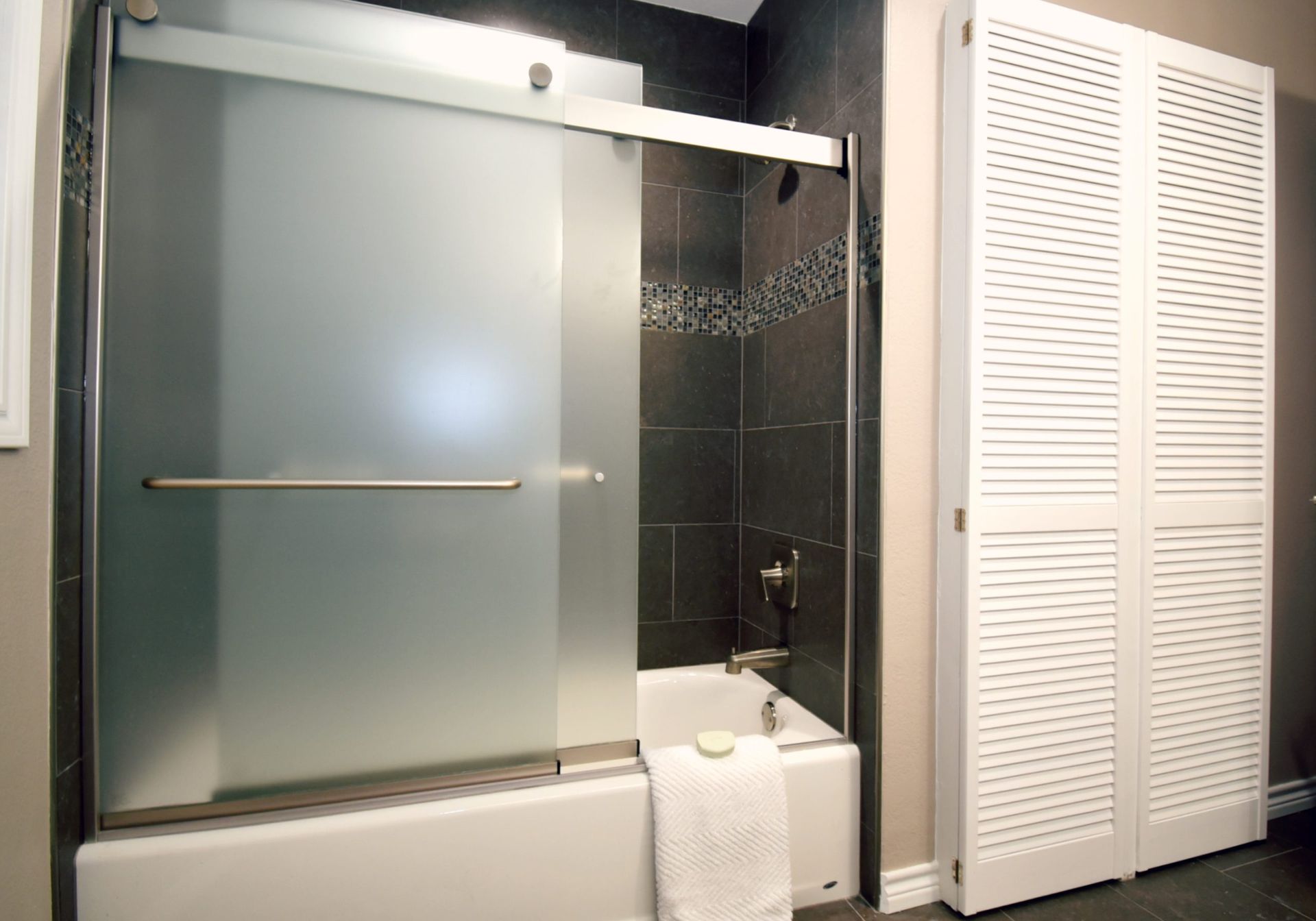 Frosted glass shower door over a bathtub with white folding doors to the right.
