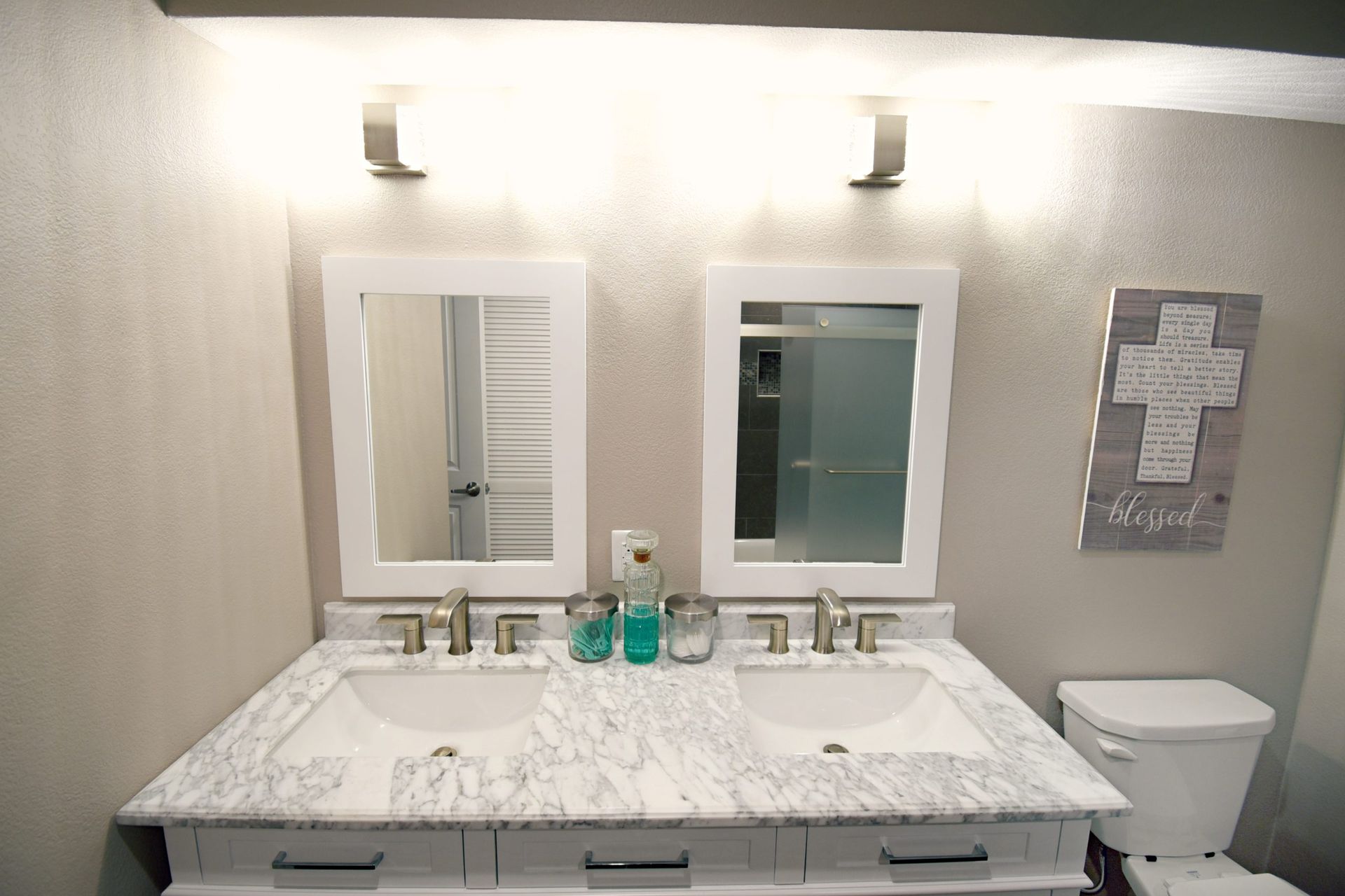 Bathroom with double vanity, white countertop, two mirrors, gray walls, and a cross decoration.