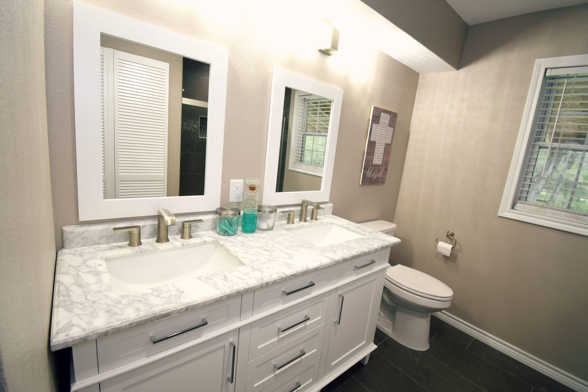 Bathroom with white double vanity, marble countertop, mirrors, and a window.