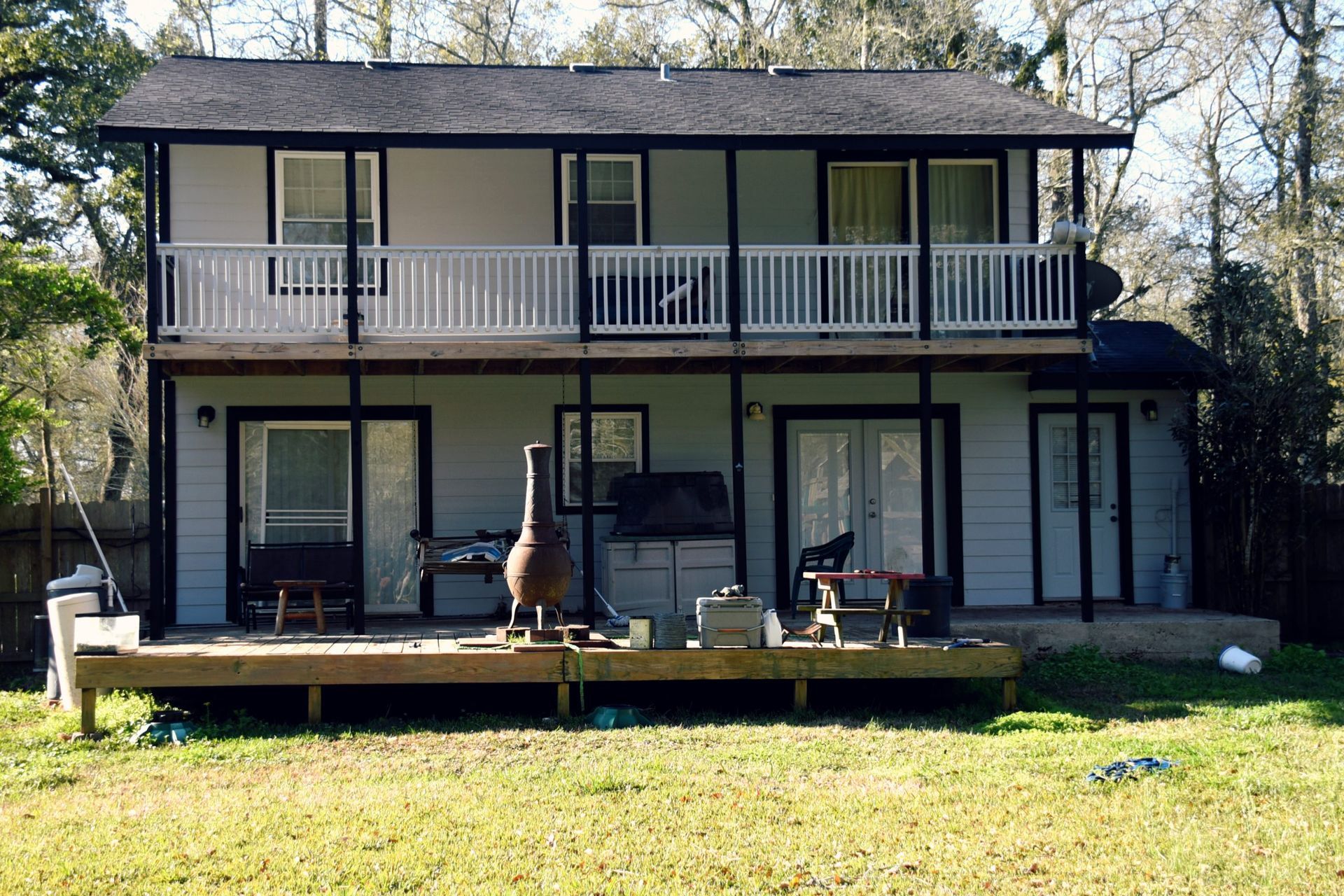 Two-story house with balconies, light blue siding, dark trim, and a wooden deck in a grassy yard.