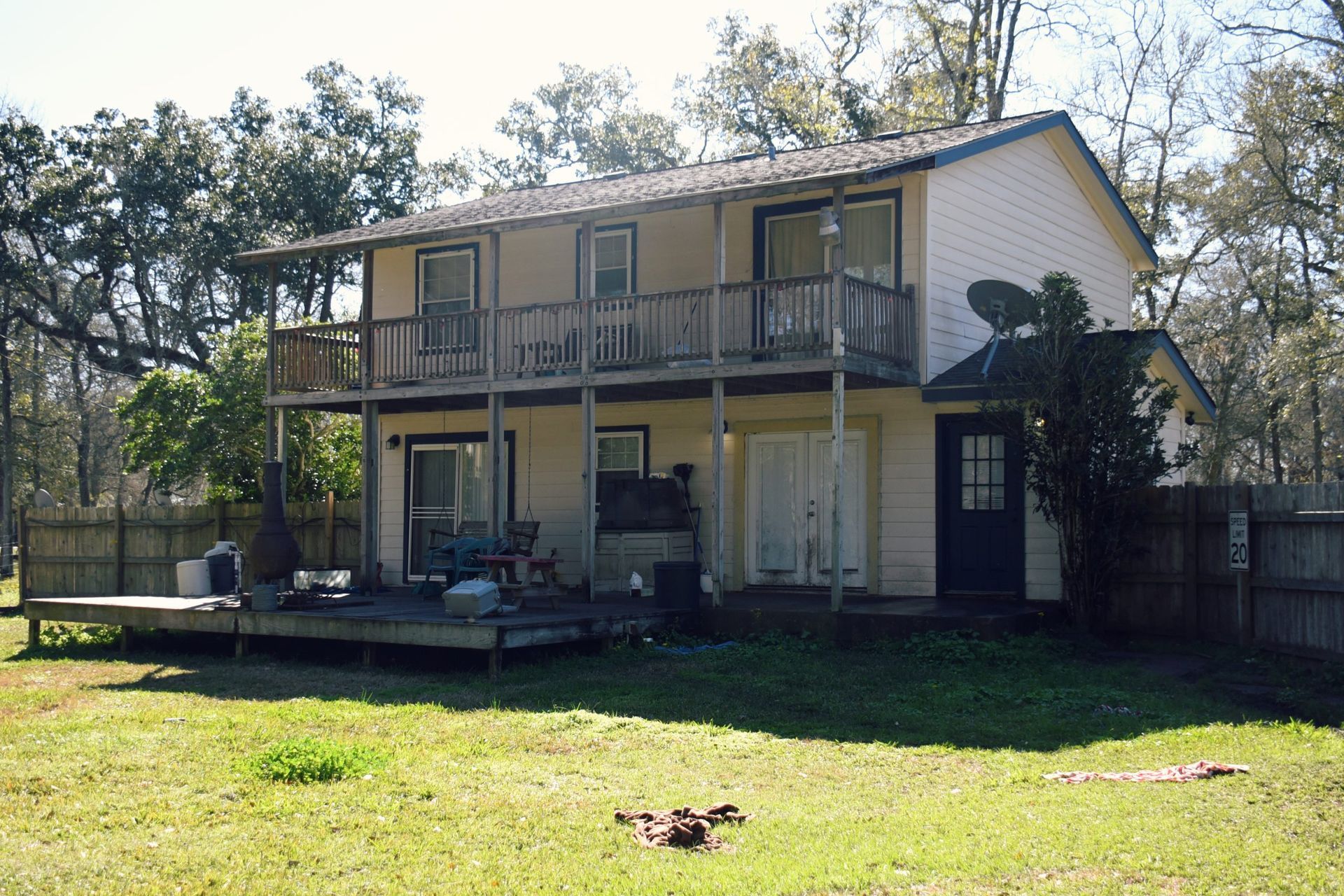 Two-story house with a deck, balconies, and a lawn, surrounded by trees and a fence.