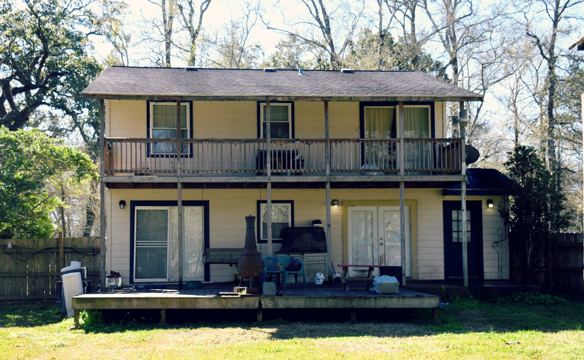 Two-story beige house with balconies, wooden deck, and backyard.