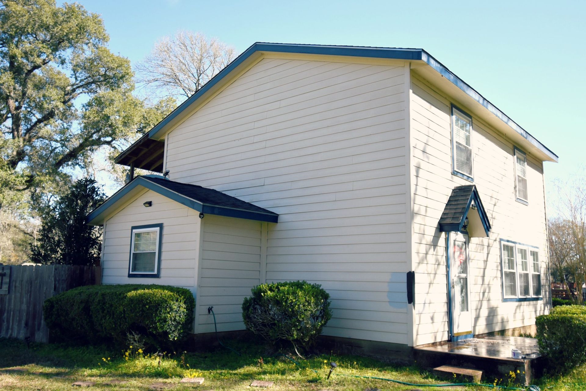 Two-story house with beige siding, dark blue trim, and small bushes in front.