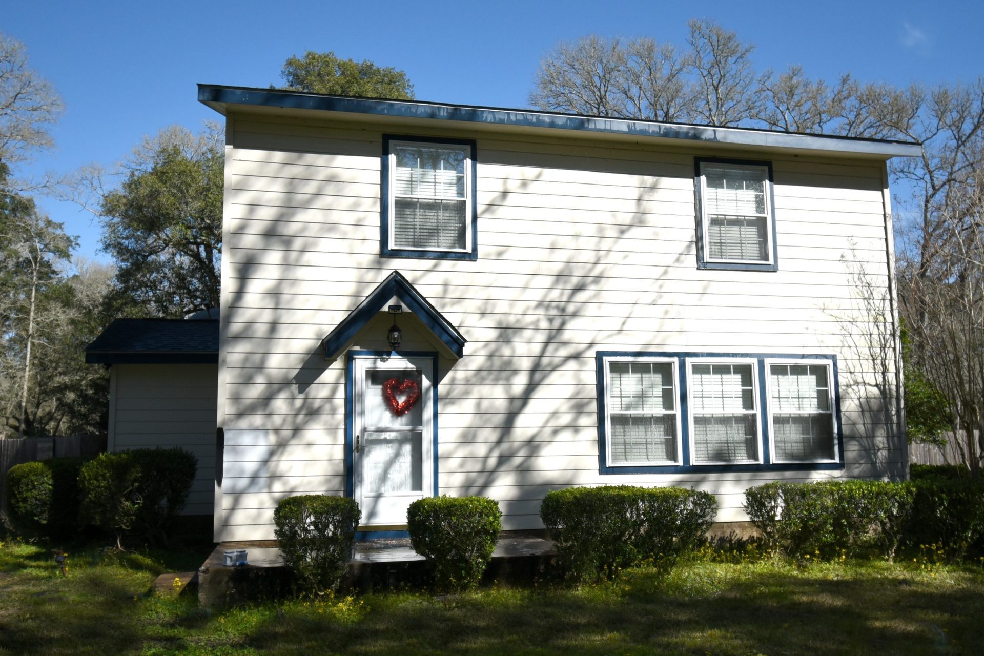 Two-story, white house with blue trim, windows, a small porch, and a heart-shaped wreath on the door.