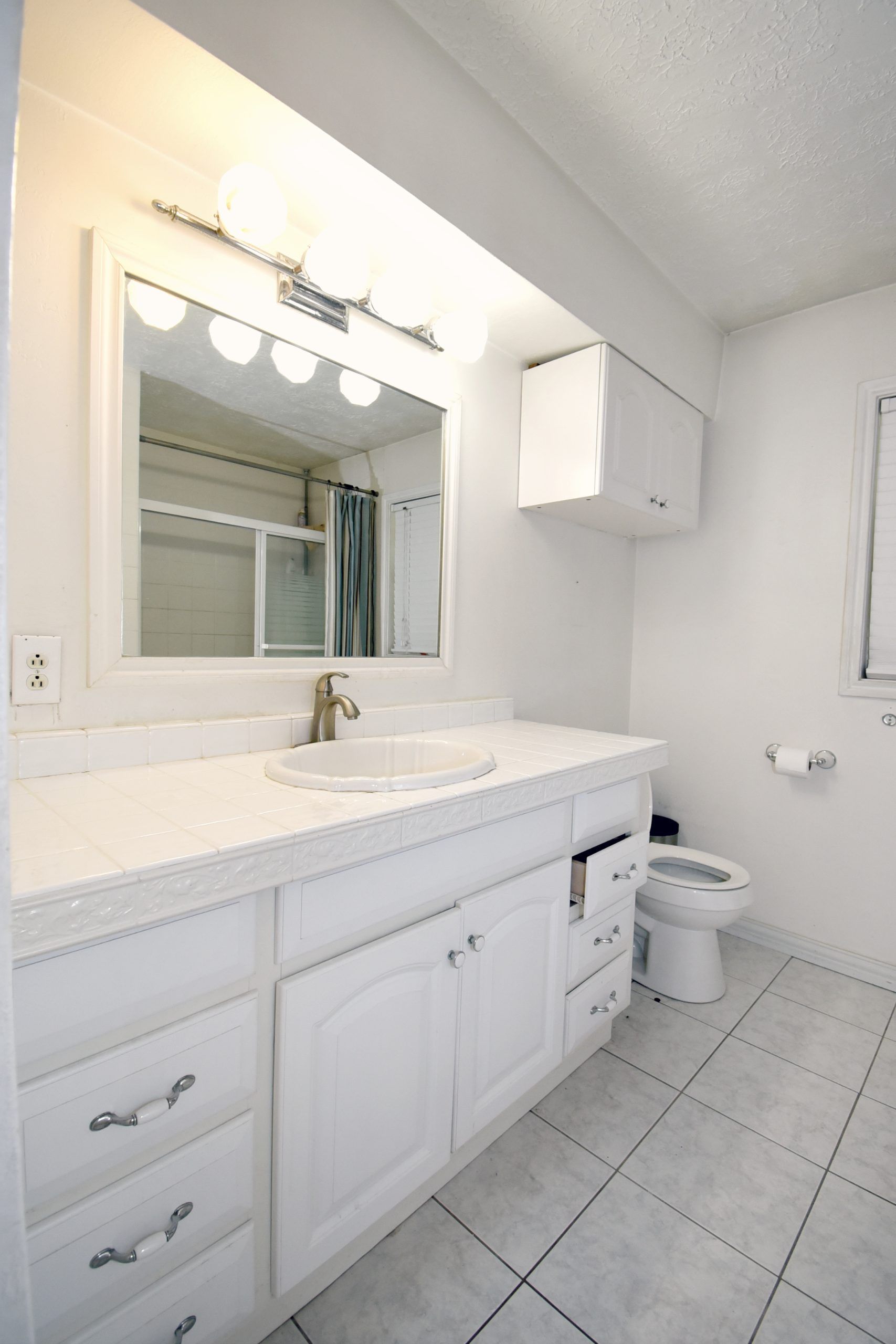 White bathroom with vanity, sink, mirror, toilet, and tiled floor.
