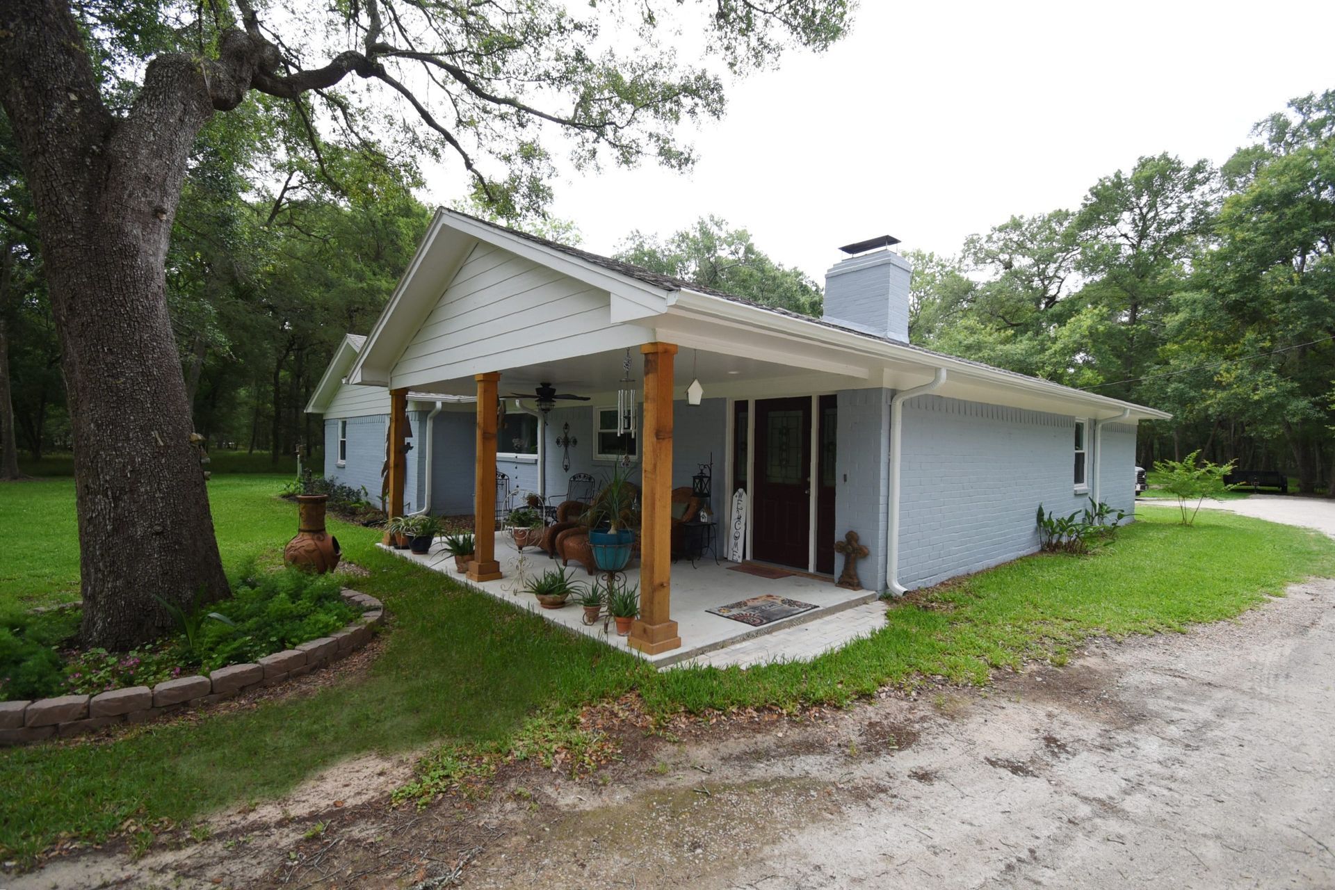 Light blue house with porch, chimney, and mature oak tree.
