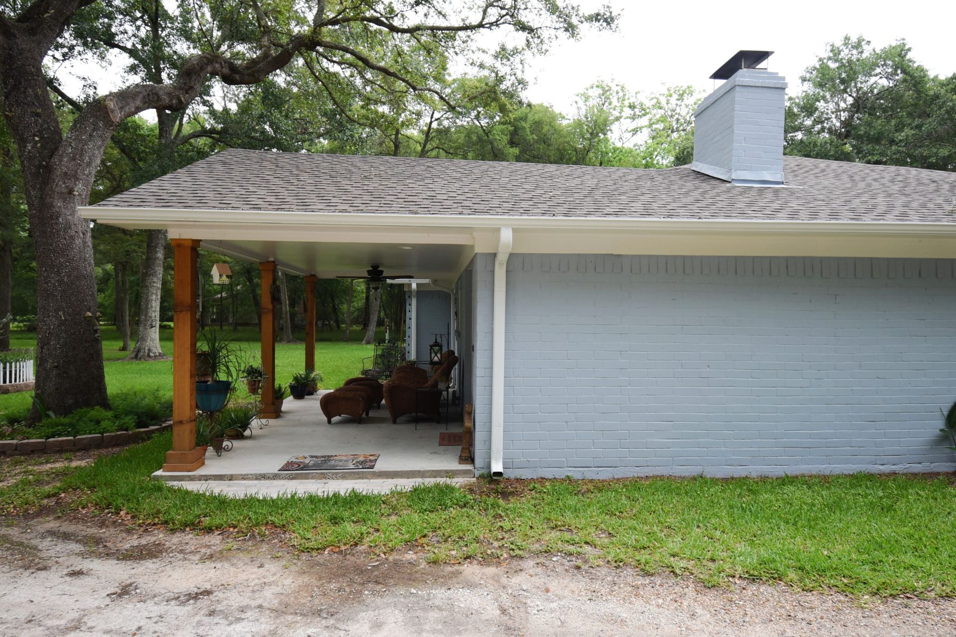 A light blue house with a porch, dogs, and trees.
