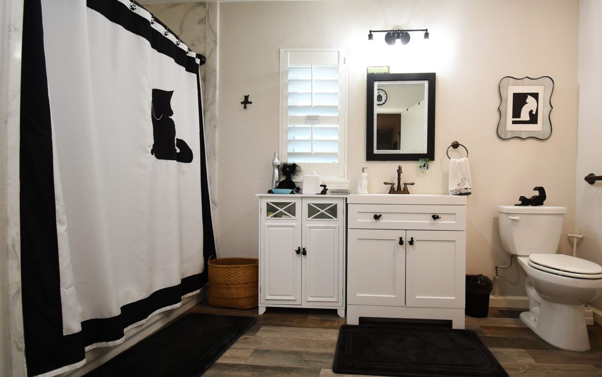 Black and white cat-themed bathroom with shower curtain, cabinet, mirror, and toilet.