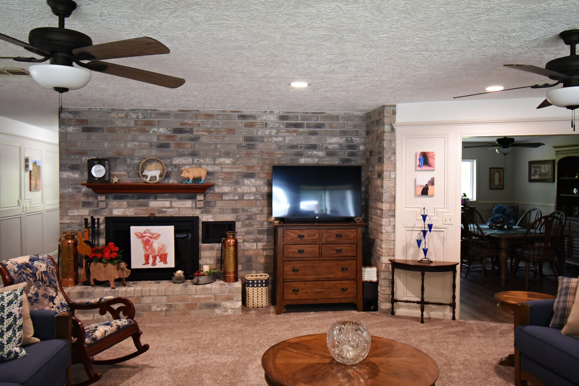 Living room with brick fireplace, TV, brown furniture, blue couches, and ceiling fans.