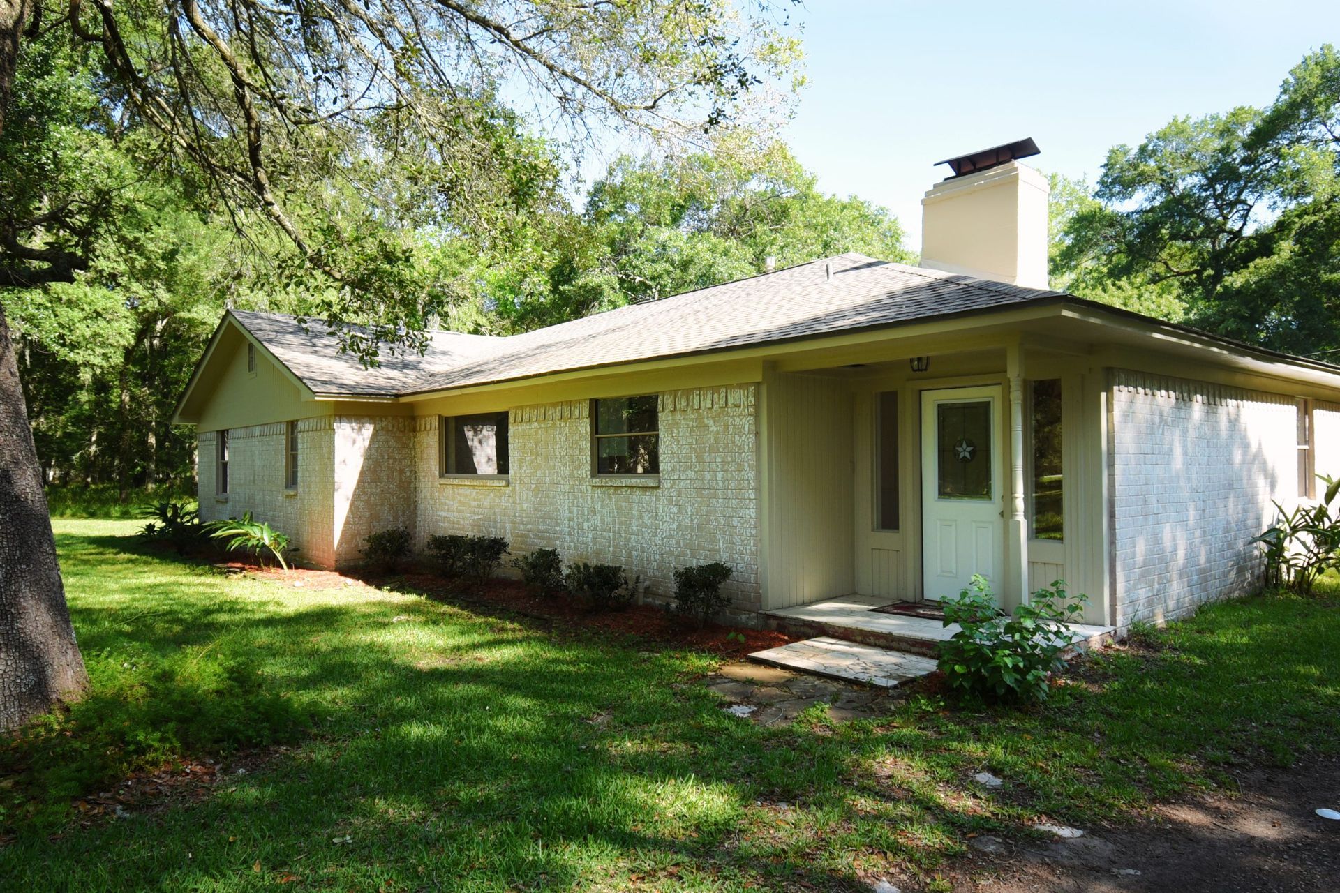 Beige ranch-style house with a chimney, small yard, and trees.