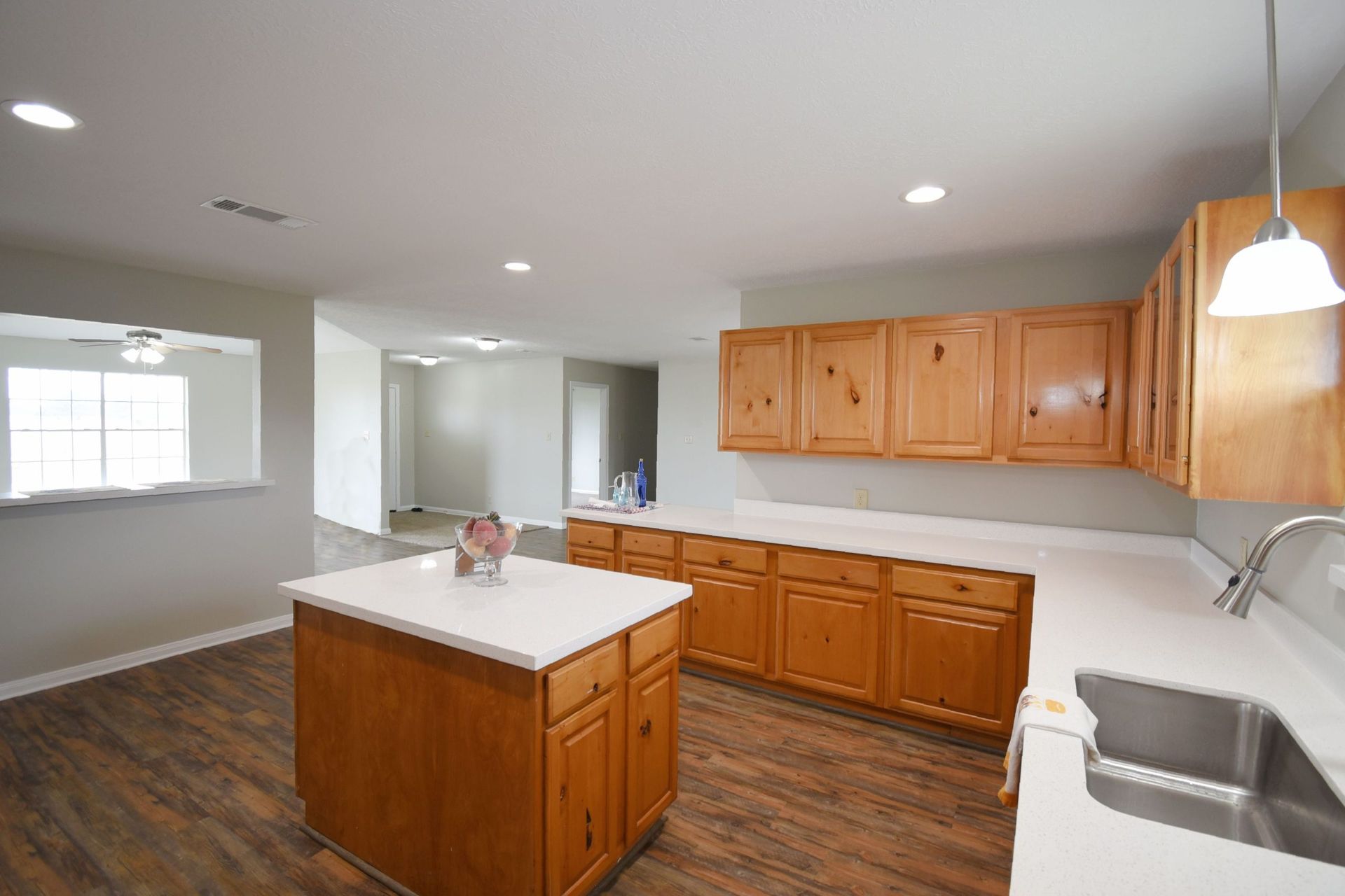Spacious kitchen with wooden cabinets, white countertops, and an island, with a view to a living space.