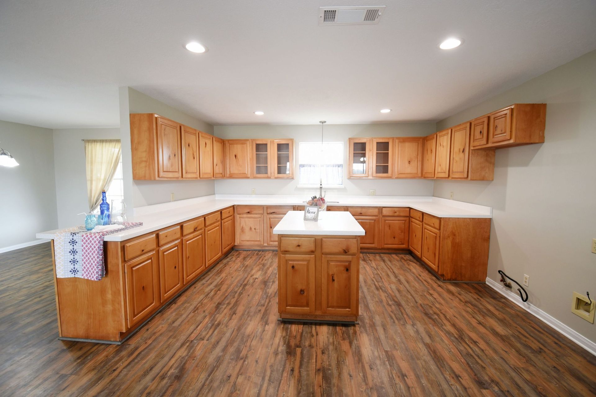 Spacious kitchen with wooden cabinets, white countertops, island, and wood-look flooring.