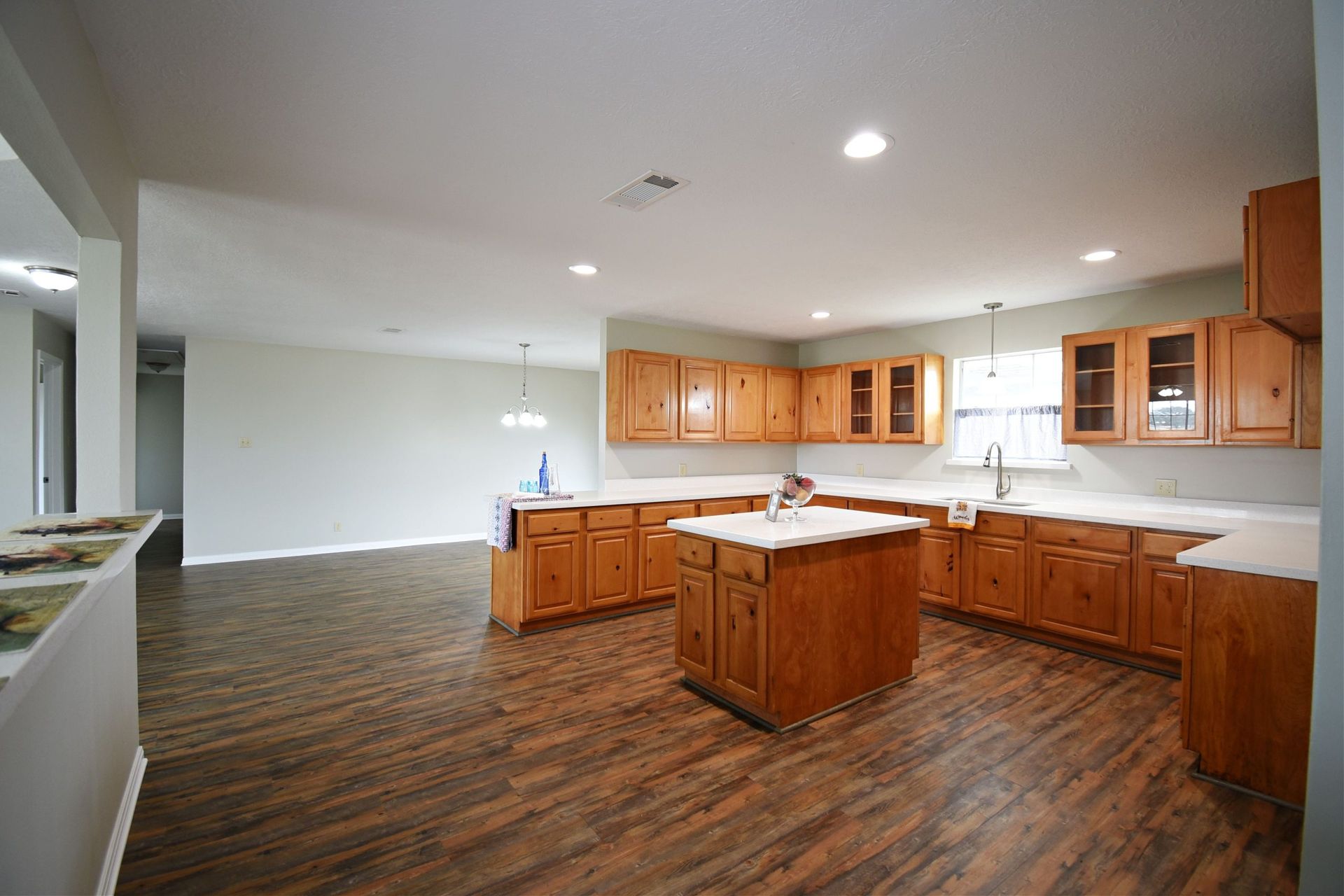 Wooden kitchen with island and cabinets, light countertops, and dark wood floor.