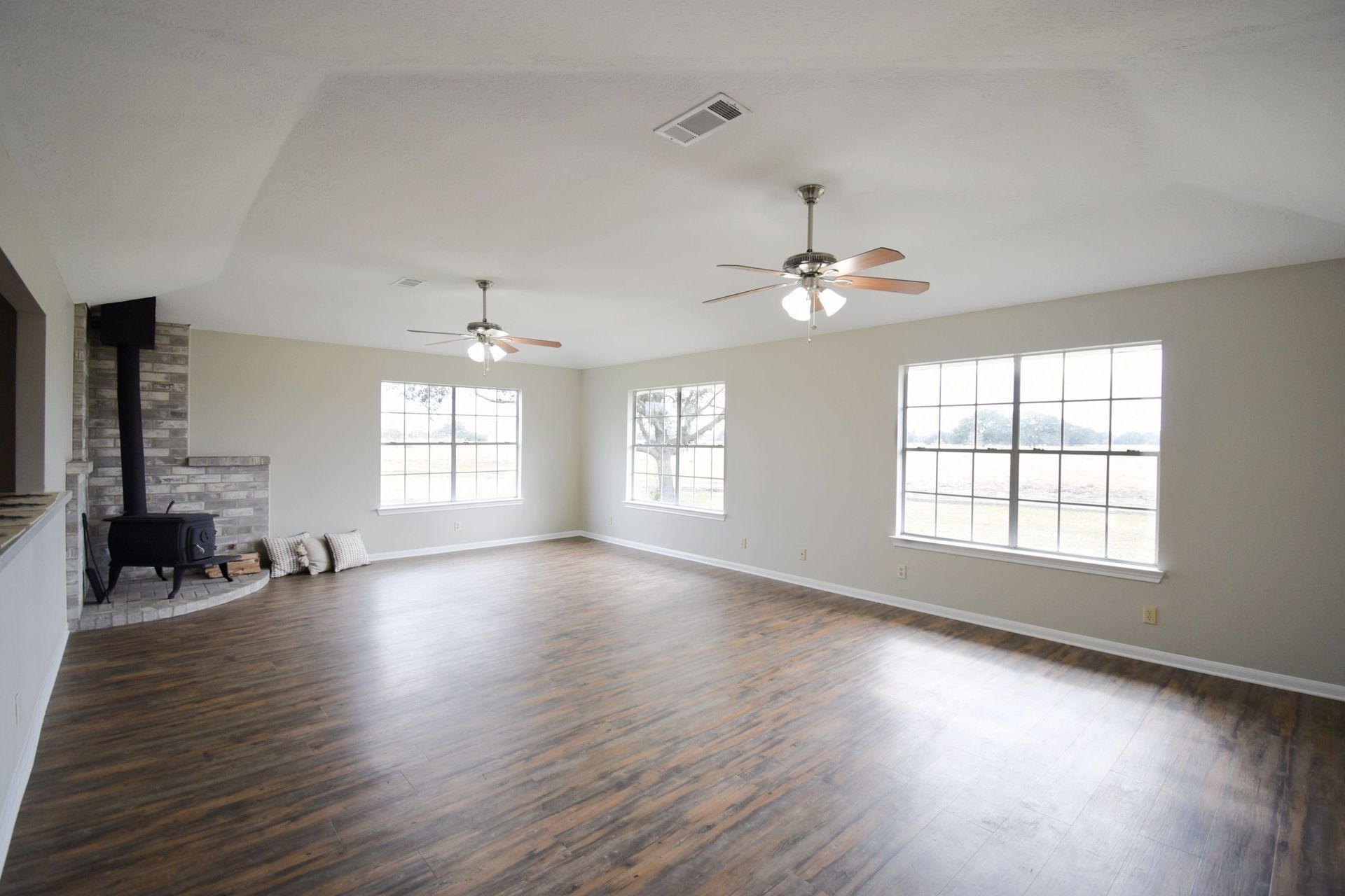 Empty living room with hardwood floors, windows, fireplace, and ceiling fans.
