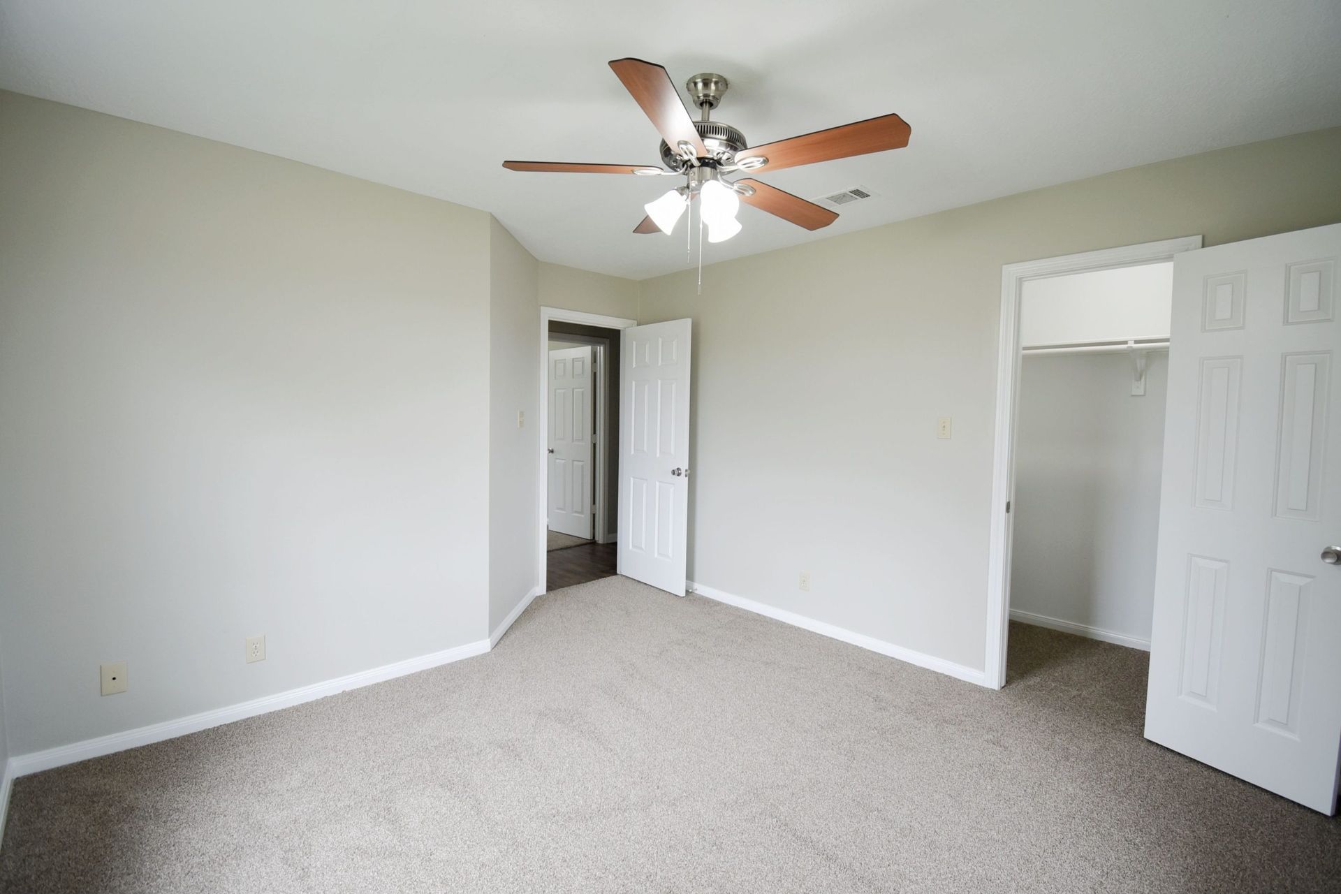 Empty bedroom with beige carpet, light gray walls, ceiling fan, and open doors.