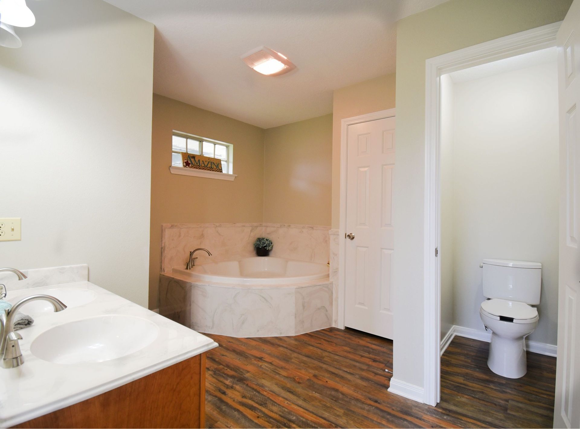 Bathroom with jacuzzi, sink, toilet. Light walls, brown floor, white accents.